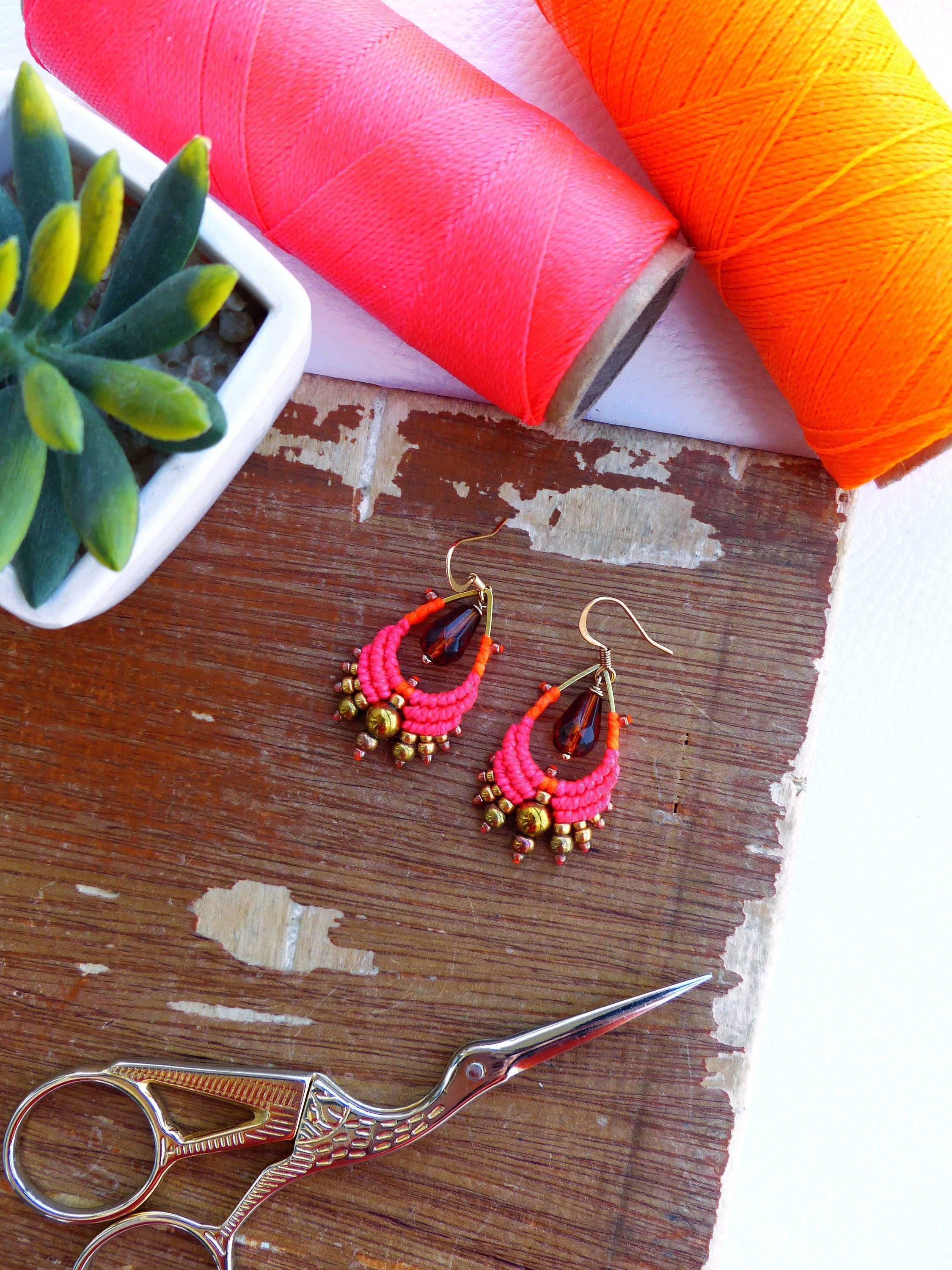 Peut inclure: Une paire de boucles d'oreilles faites à la main avec des perles roses et orange, des perles en verre brun et des accents dorés. Les boucles d'oreilles sont suspendues à des crochets dorés.