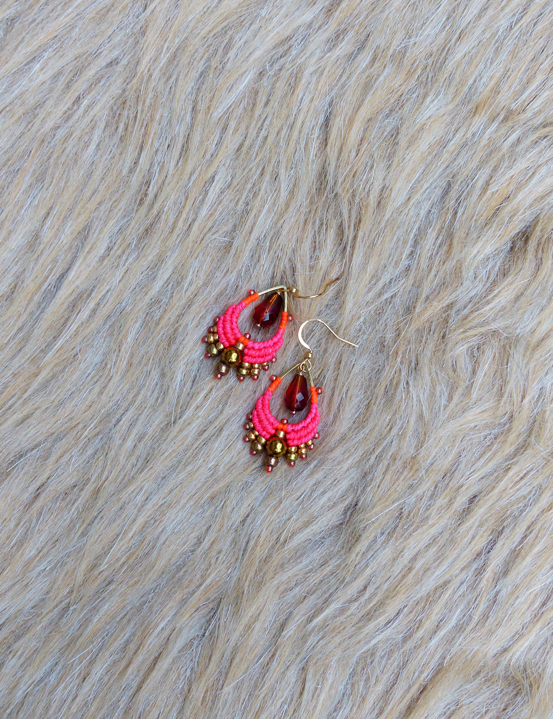 Peut inclure: Une paire de boucles d'oreilles en perles roses et dorées avec une perle de verre rouge en forme de larme au centre de chaque boucle d'oreille.