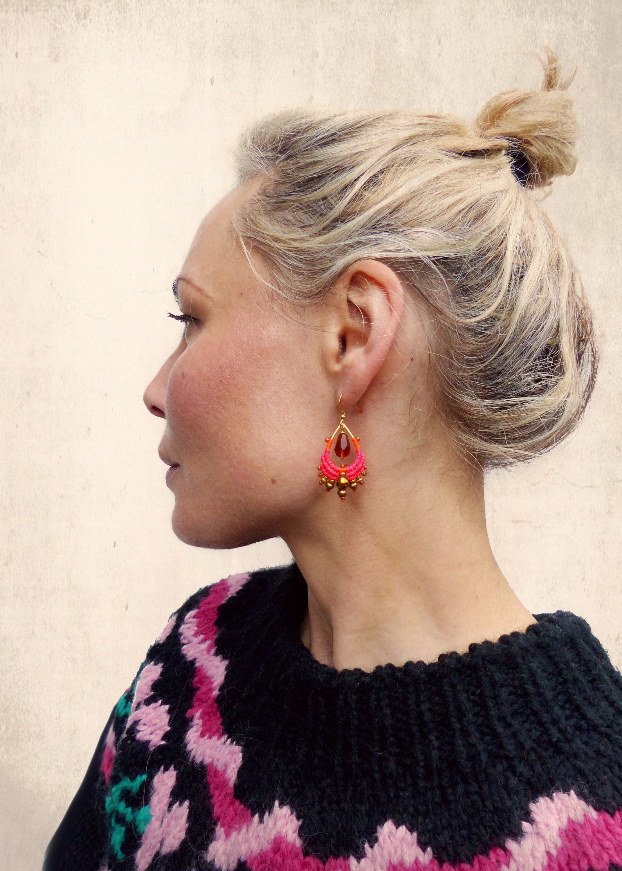 Peut inclure: Une femme portant un pull noir et rose avec des boucles d'oreilles pendantes roses et dorées. Les boucles d'oreilles présentent une pierre rouge en forme de larme.
