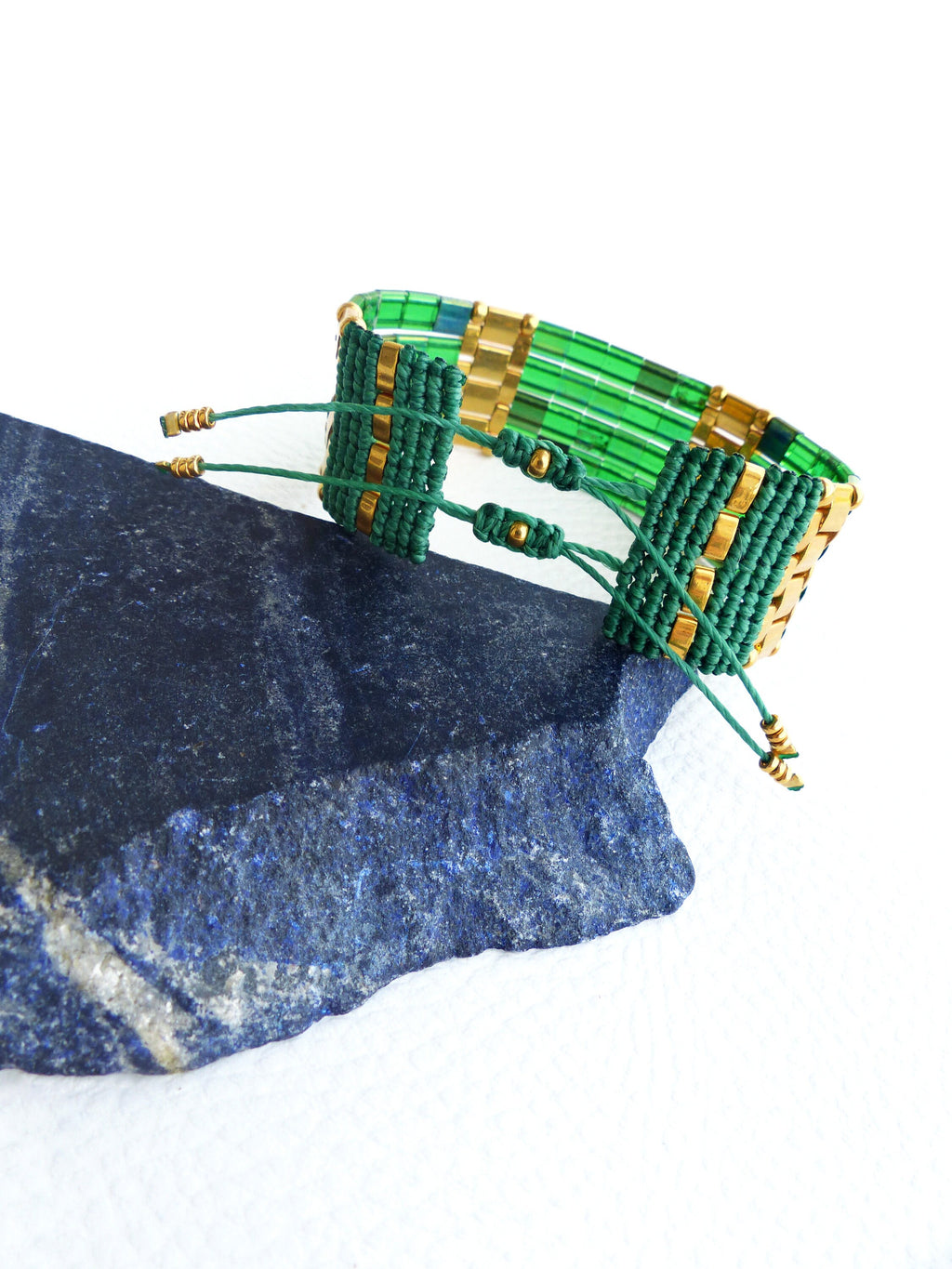 Peut inclure: Un bracelet en perles vertes et dorées avec un motif tissé. Le bracelet est noué avec une ficelle et a des perles dorées aux extrémités.