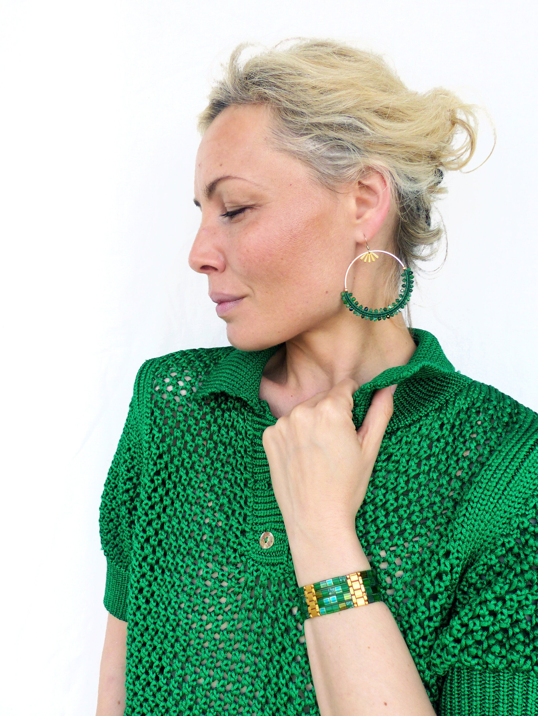 Peut inclure: Une femme portant un pull en tricot vert avec un bracelet en perles vertes et dorées et des boucles d'oreilles créoles en perles vertes et dorées.