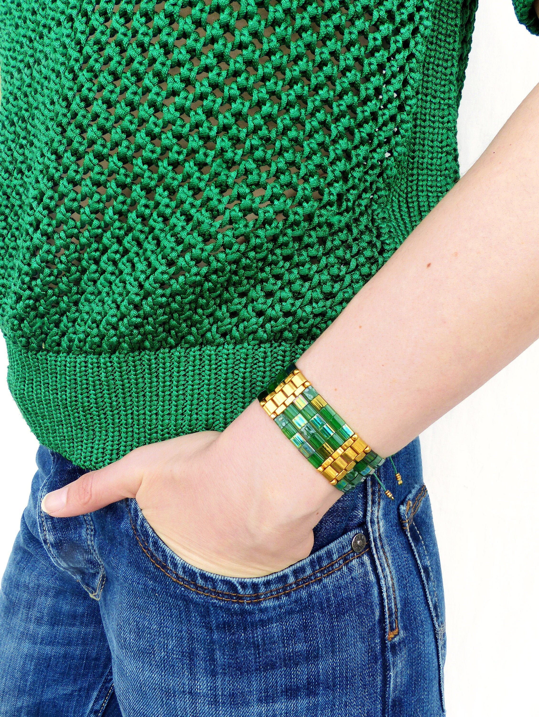 Peut inclure: Un bracelet vert et or avec un motif géométrique. Le bracelet est composé de petites tuiles carrées disposées en un motif répétitif. Les tuiles sont un mélange de vert et d'or, et le bracelet est sécurisé par un fermoir en or.