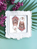 Peut inclure: Une paire de boucles d'oreilles en perles roses et dorées avec un design en frange. Les boucles d'oreilles sont présentées dans un cadre blanc à motif floral.