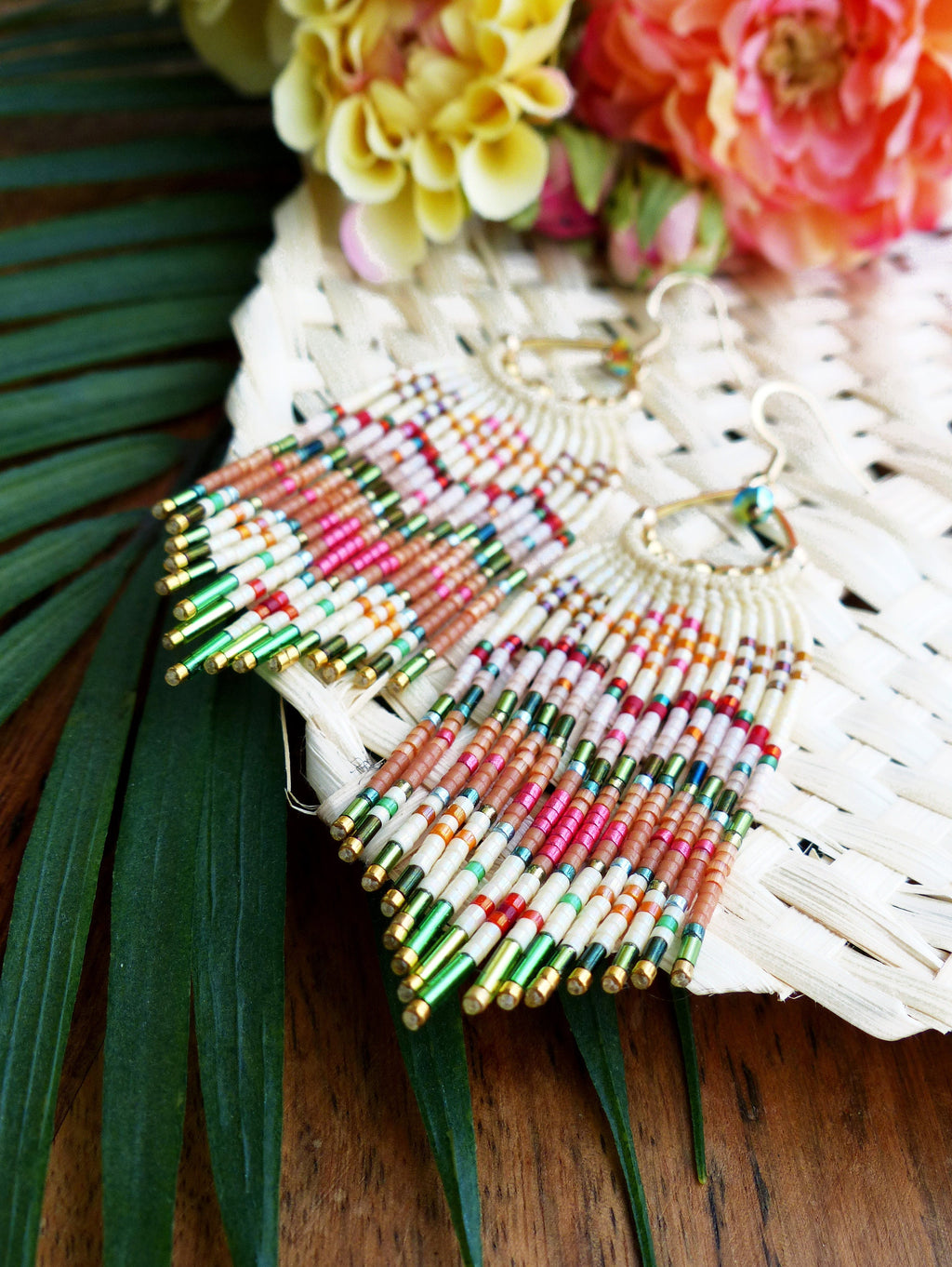 Peut inclure: Une paire de longues boucles d'oreilles en perles avec un design en frange. Les boucles d'oreilles sont faites de perles blanches, roses, orange et vertes. Les boucles d'oreilles sont suspendues à des crochets dorés.
