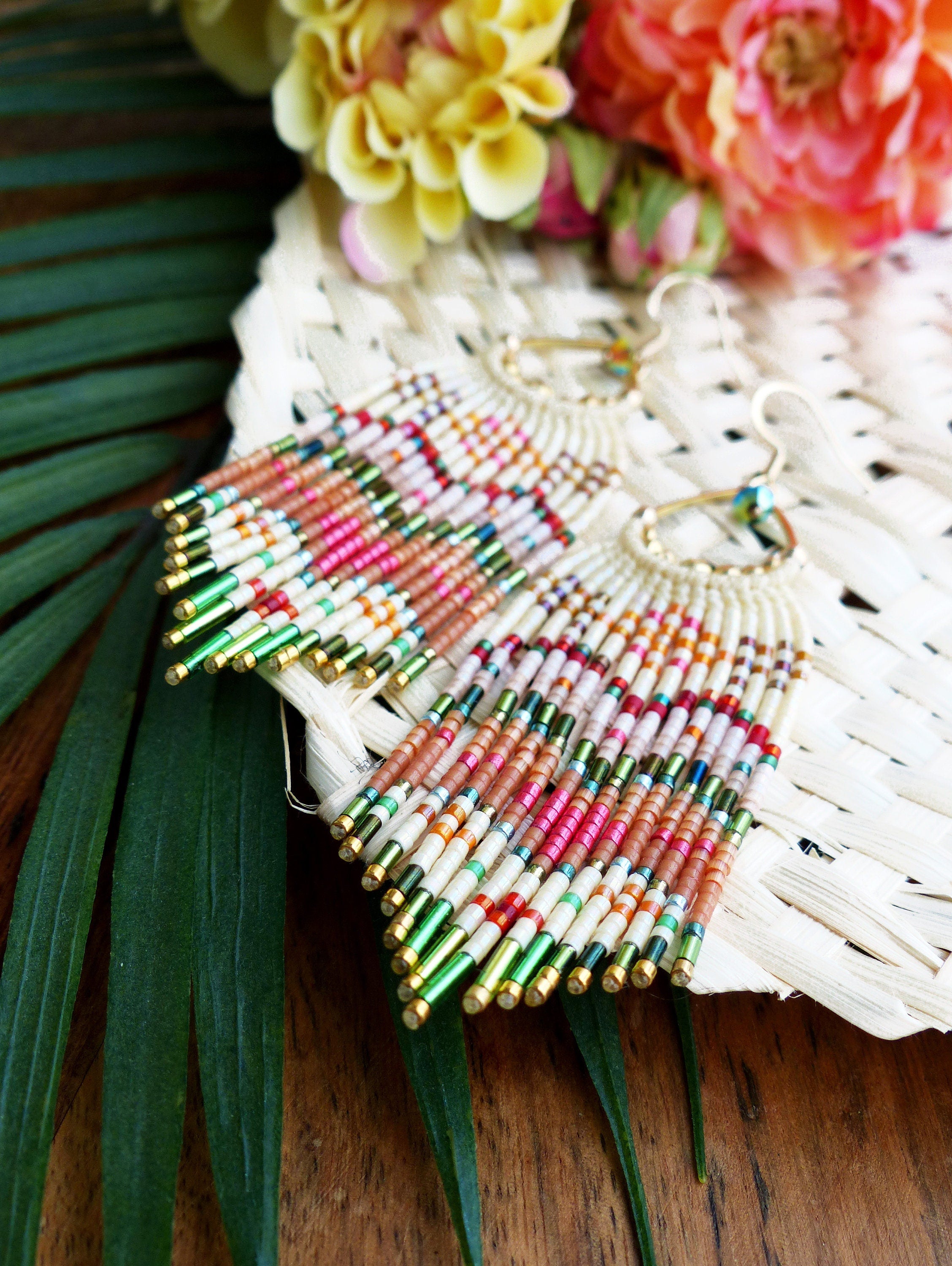 Peut inclure: Une paire de longues boucles d'oreilles en perles avec un design en frange. Les boucles d'oreilles sont faites de perles blanches, roses, orange et vertes. Les boucles d'oreilles sont suspendues à des crochets dorés.