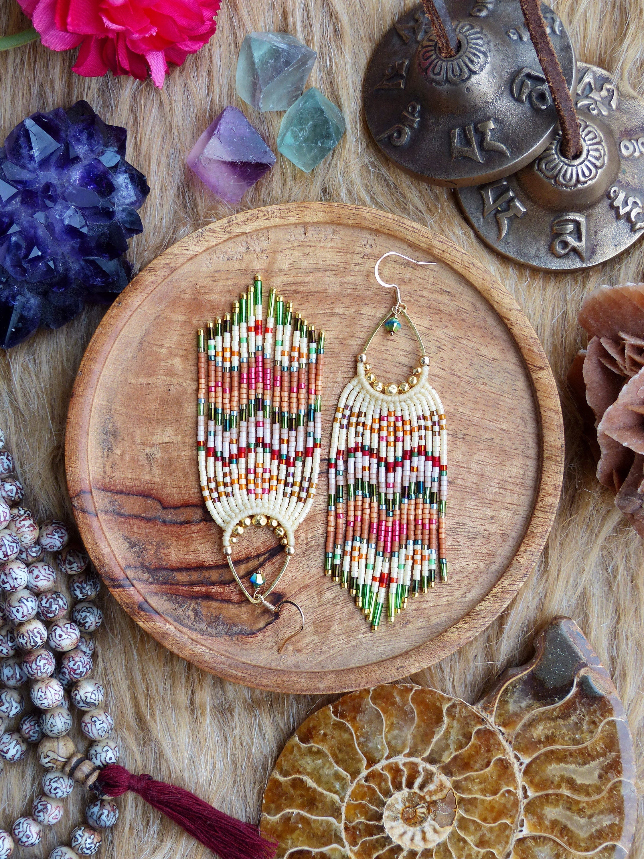 Peut inclure: Une paire de longues boucles d'oreilles en perles avec un motif géométrique dans des tons de vert, rouge, blanc et or. Les boucles d'oreilles sont suspendues à une assiette en bois.