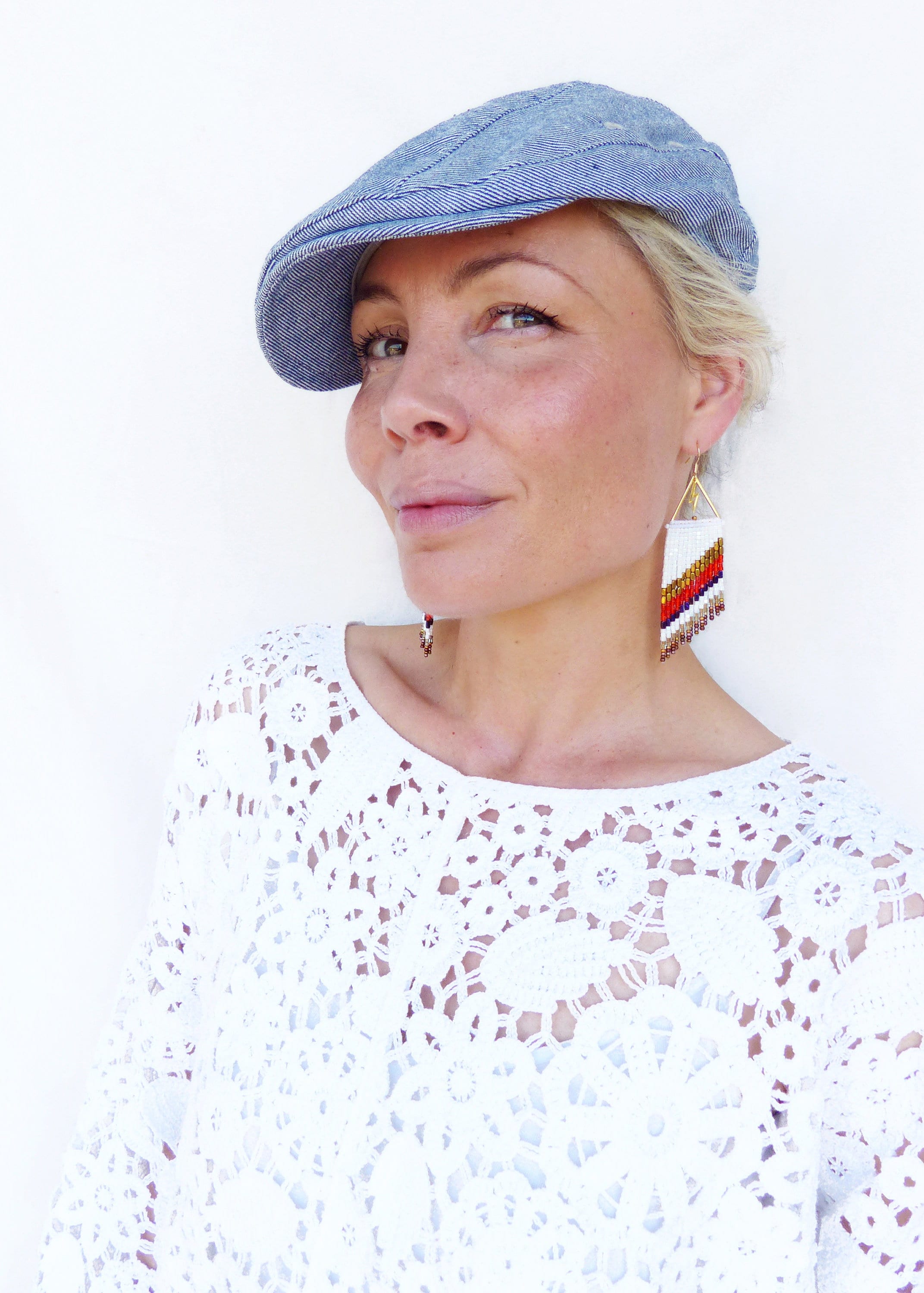 Peut inclure: Une femme portant un haut en crochet blanc et une casquette de newsboy en denim bleu. Elle porte de longues boucles d'oreilles en perles blanches, rouges, orange et brunes.