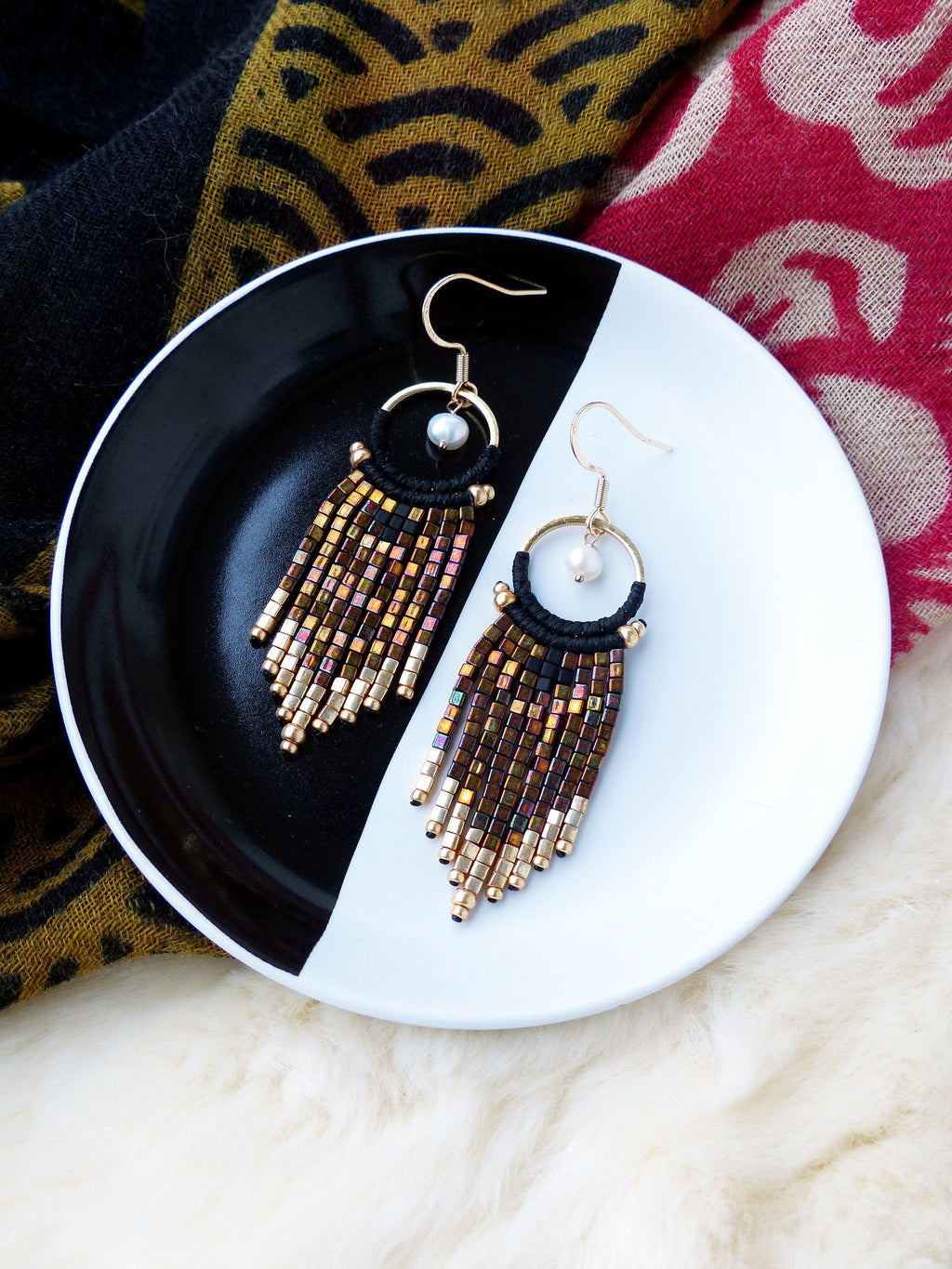 Peut inclure: Une paire de boucles d'oreilles créoles dorées avec du fil noir et des perles brunes et dorées qui pendent des créoles. Chaque boucle d'oreille a un petit charme de perle blanche.