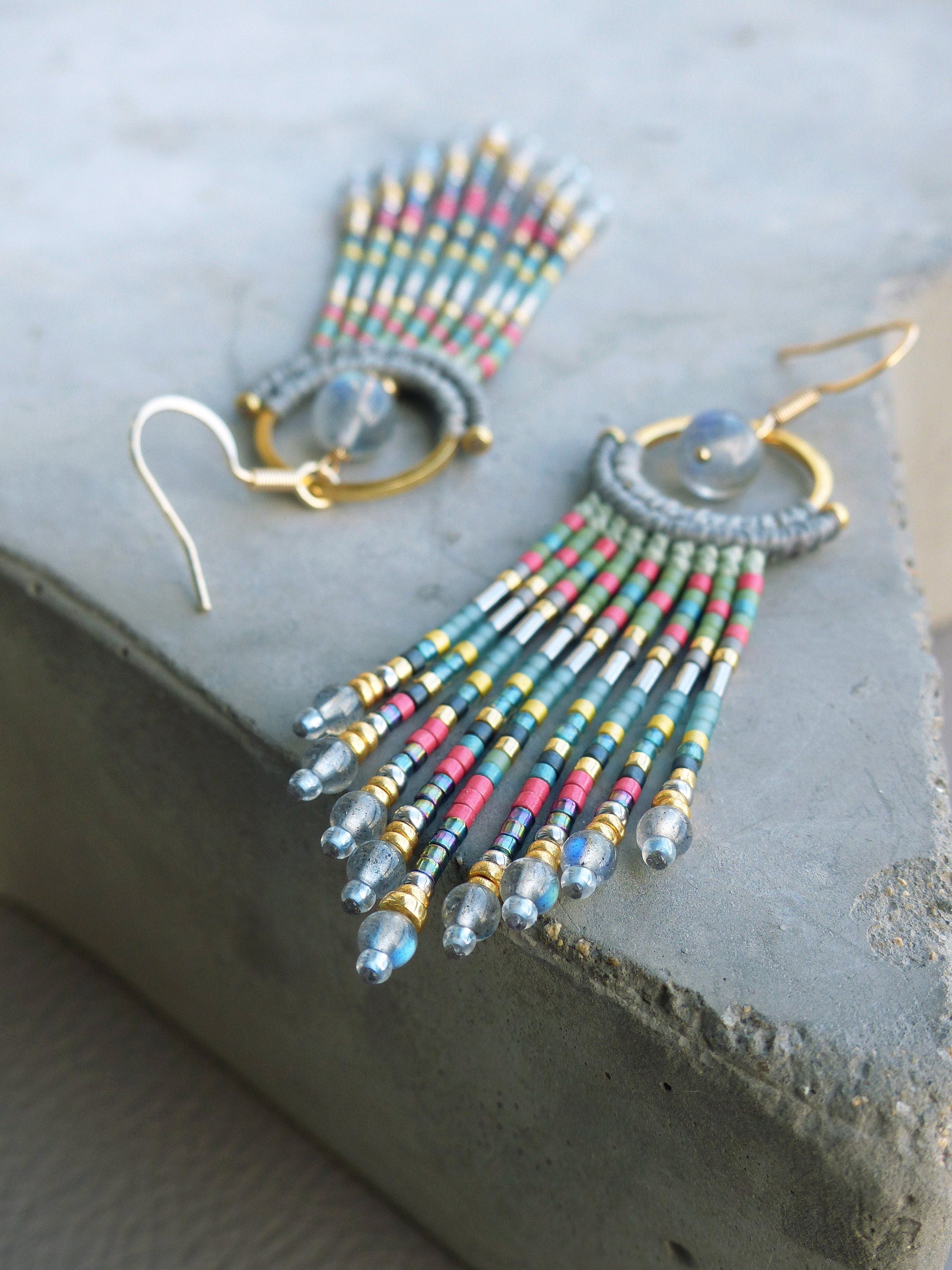 Peut inclure: Une paire de longues boucles d'oreilles en perles avec un anneau en or et une pierre en forme de larme. Les perles sont dans des tons de bleu, vert, rose et or.