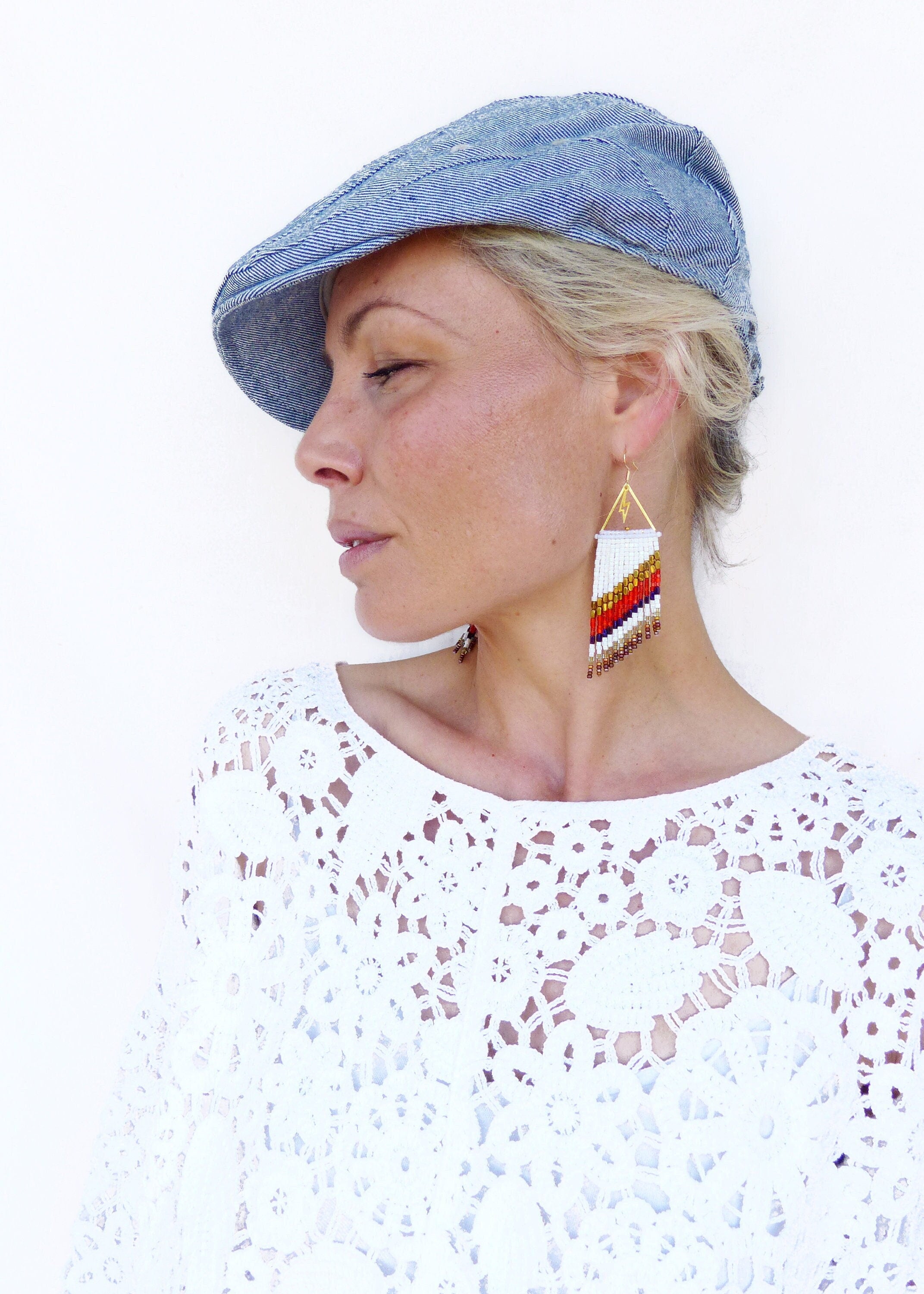 Peut inclure: Une femme portant un haut en crochet blanc et une casquette de newsboy en denim bleu. Elle porte de longues boucles d'oreilles en perles de couleur blanche, rouge et or.