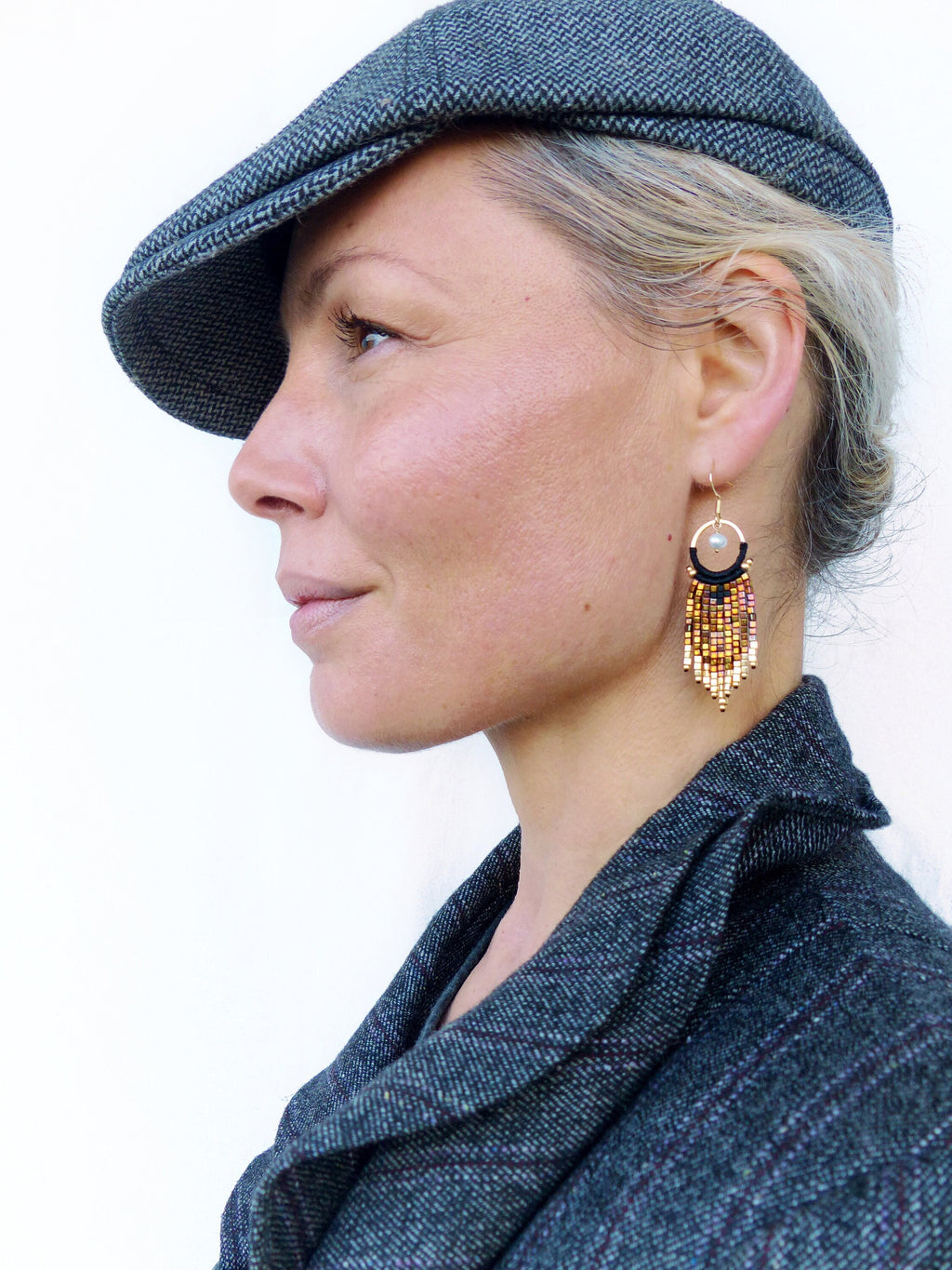 Peut inclure: Une femme portant une casquette de newsboy en tweed gris et une veste en tweed gris avec une boucle d'oreille à franges en perles noires et dorées.