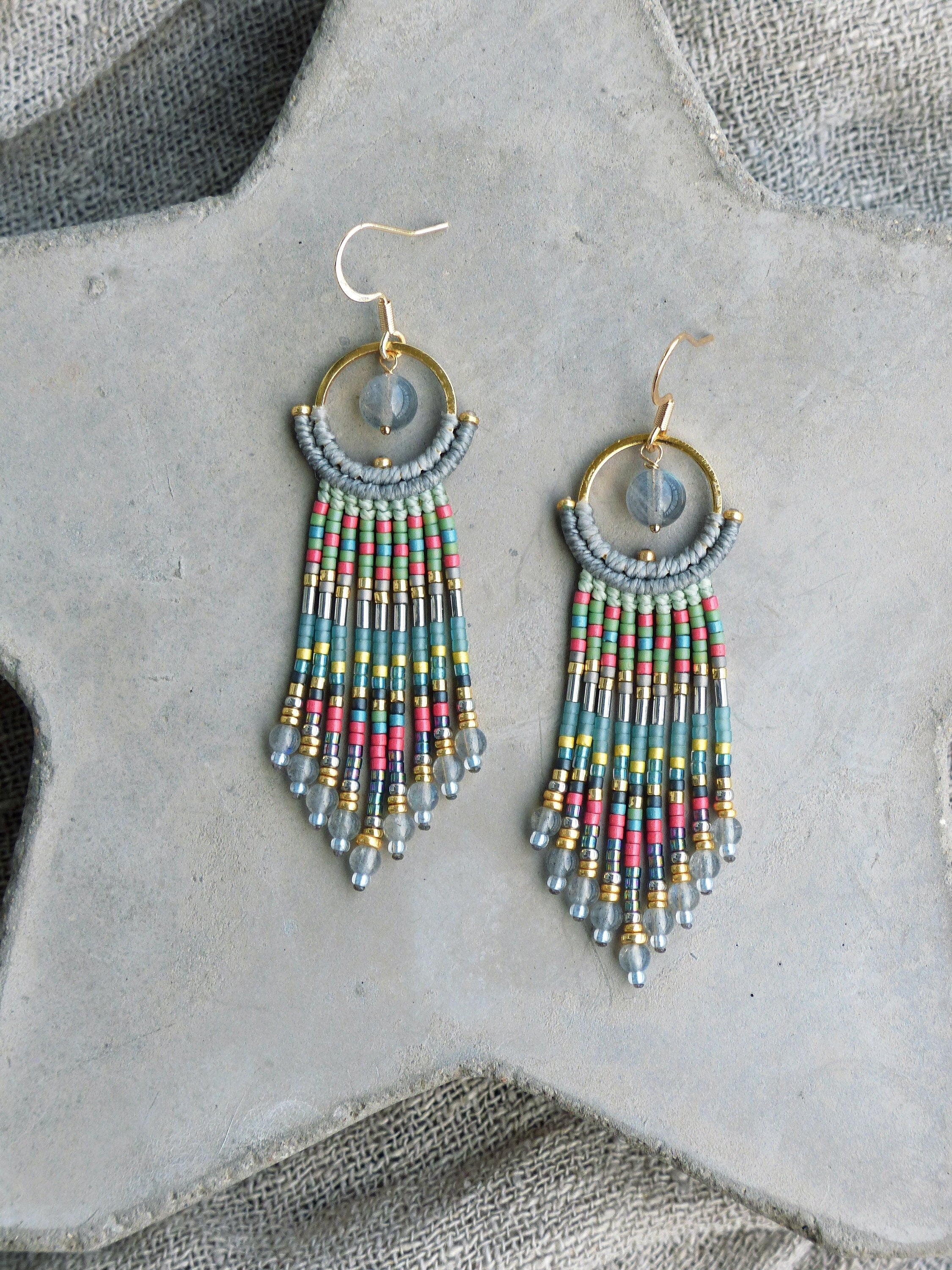 Peut inclure: Une paire de longues boucles d'oreilles pendantes en perles avec un anneau en or et une pierre transparente en haut. Les perles sont dans des tons de bleu, vert, rose et argent.