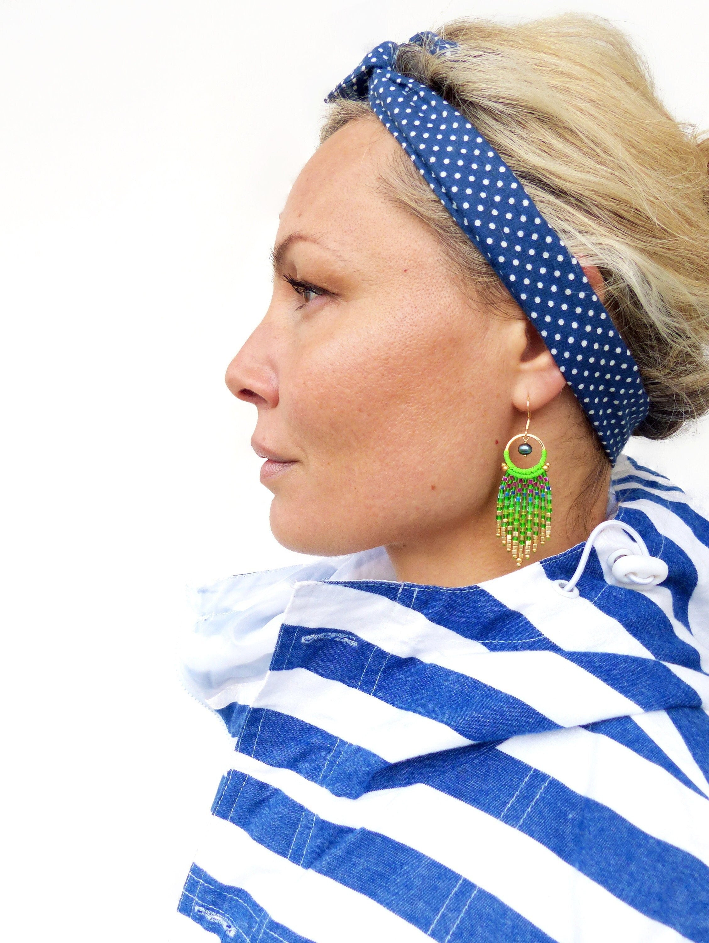 Peut inclure: Une femme porte un bandeau bleu marine à pois blancs et des boucles d'oreilles en perles vertes et dorées. Elle porte également une chemise à rayures bleues et blanches.