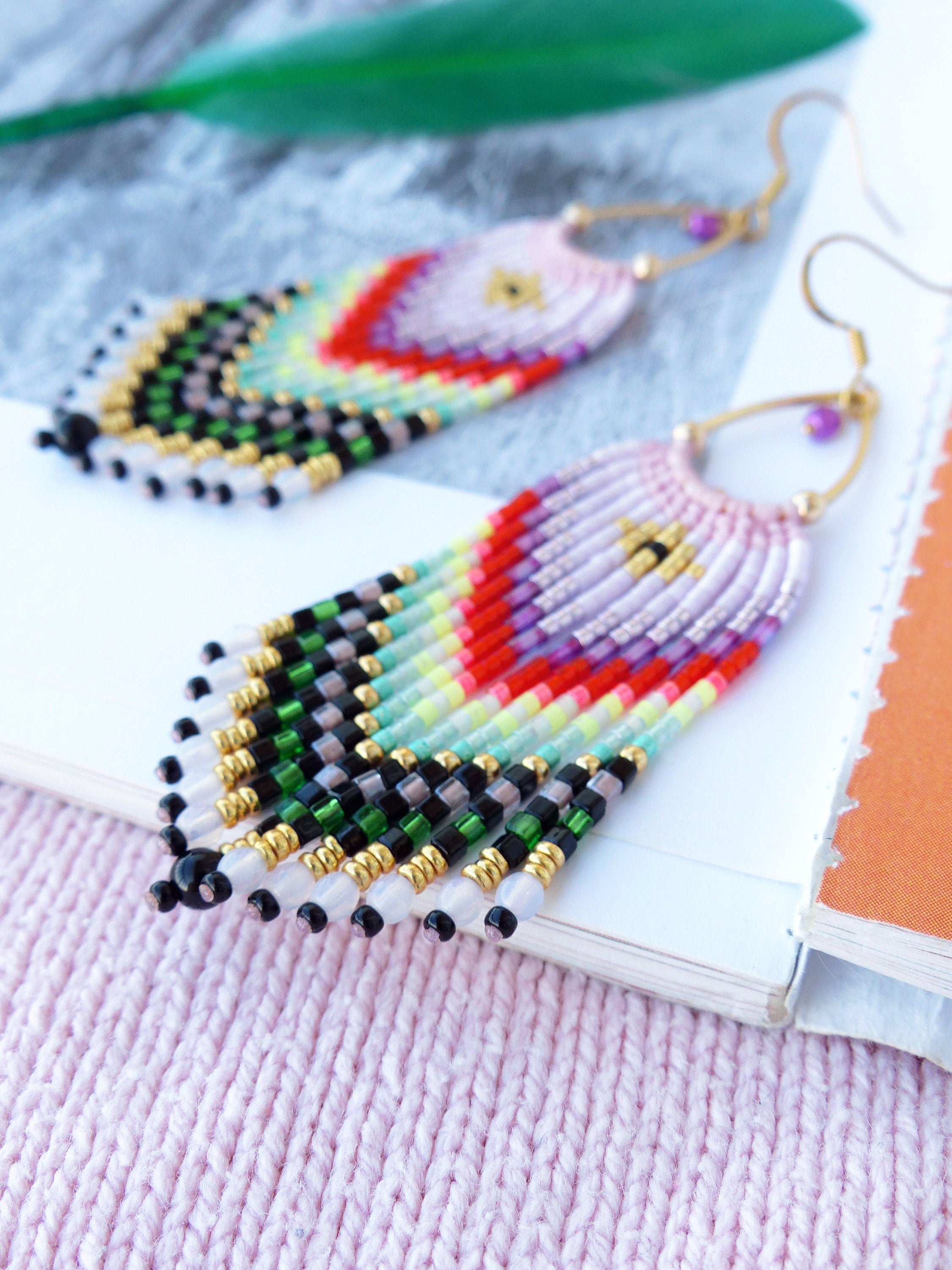 Peut inclure: Une paire de boucles d'oreilles en perles colorées avec un motif géométrique. Les boucles d'oreilles sont faites de petites perles colorées et ont une fermeture à crochet dorée.