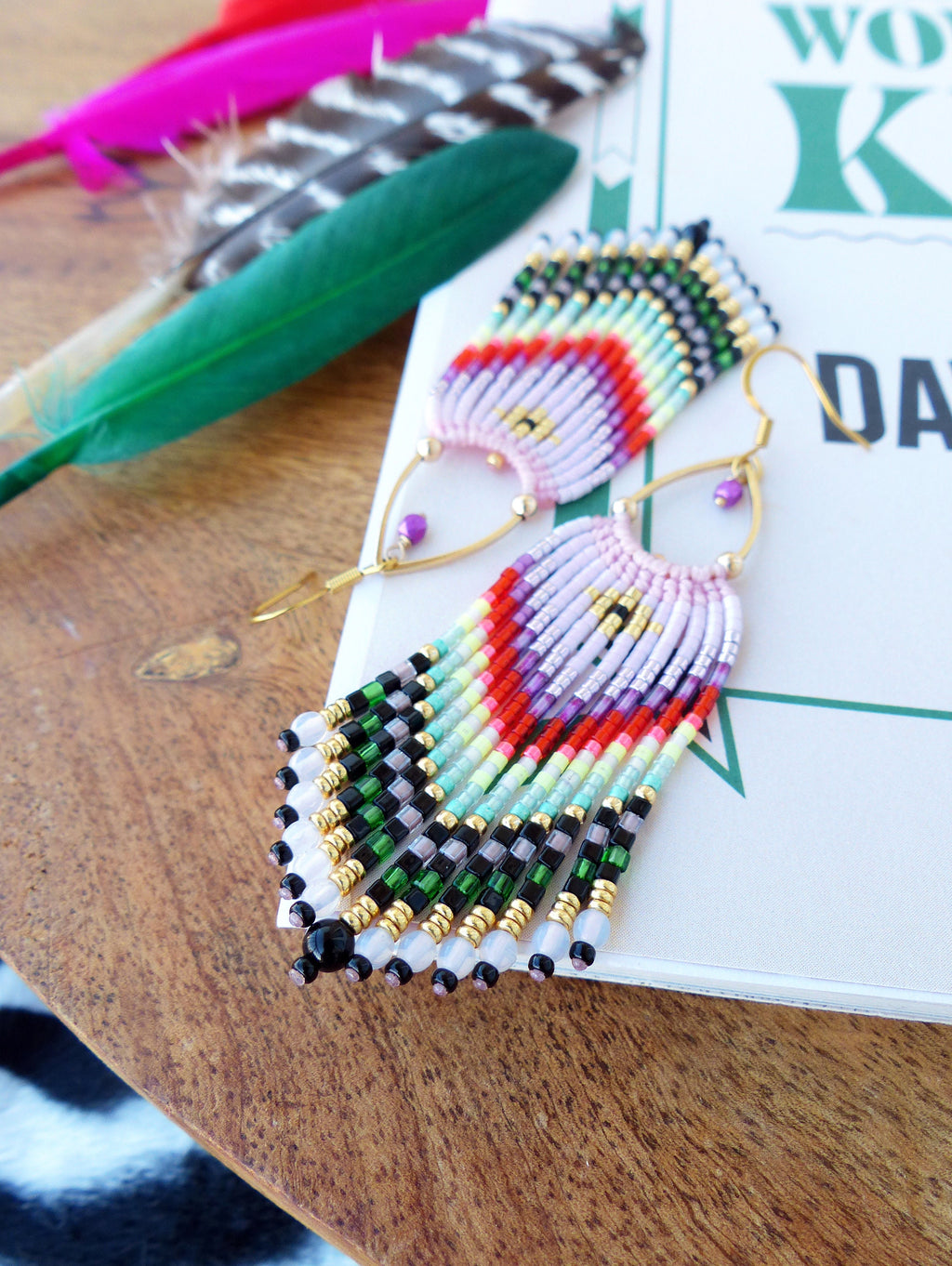 Peut inclure: Une paire de longues boucles d'oreilles en perles colorées avec des anneaux dorés. Les boucles d'oreilles présentent un arc-en-ciel de couleurs, notamment le rose, le rouge, l'orange, le jaune, le vert, le bleu et le violet. Les perles sont disposées selon un motif géométrique, créant un design unique et accrocheur.
