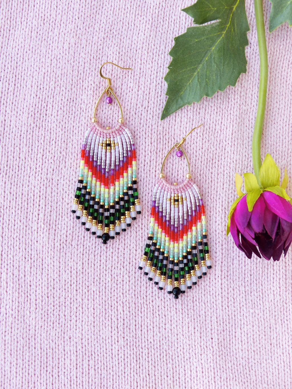 Peut inclure: Une paire de boucles d'oreilles en perles colorées avec un design en frange. Les boucles d'oreilles sont faites de petites perles colorées et ont une fermeture à crochet dorée.