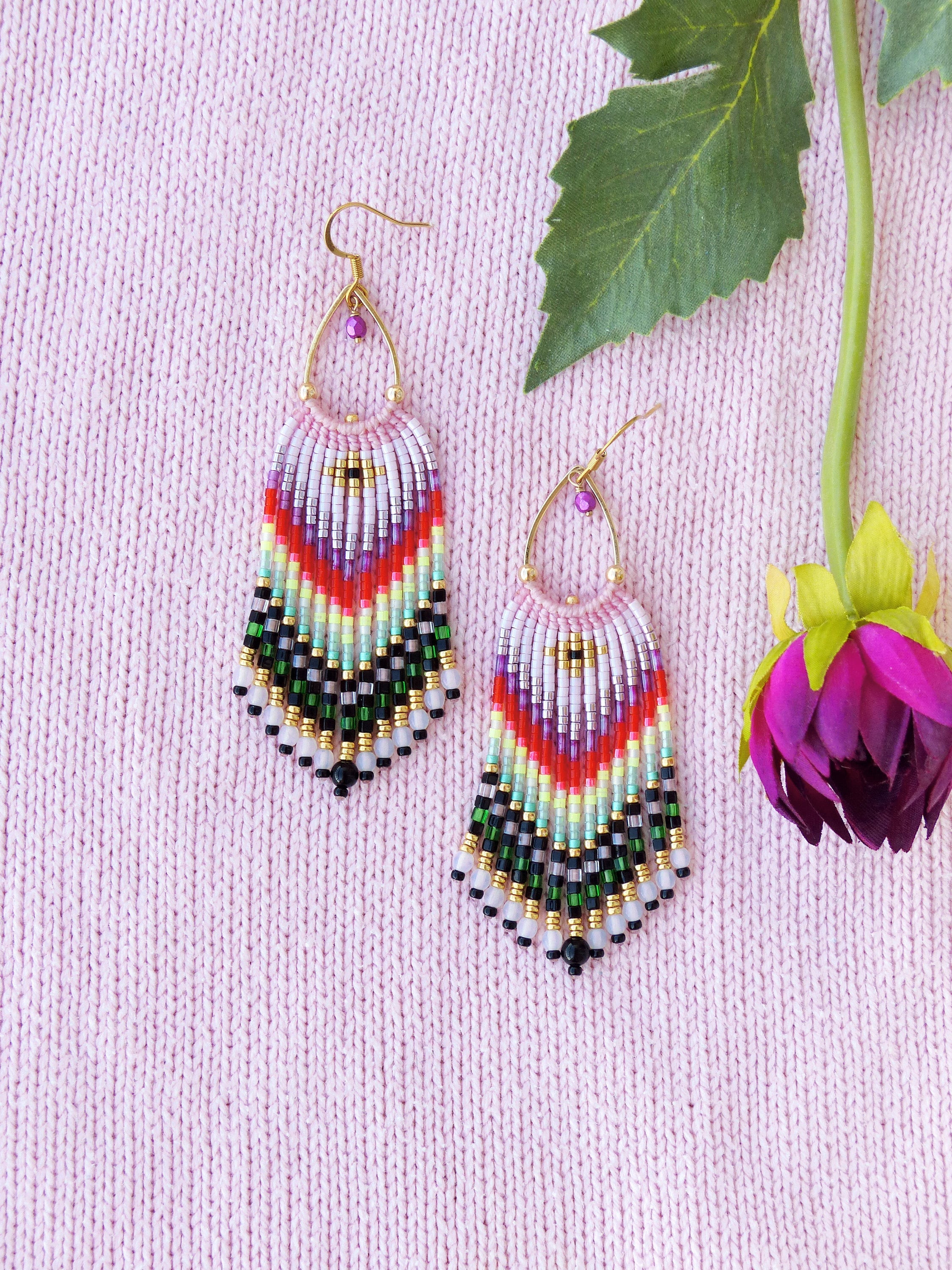 Peut inclure: Une paire de boucles d'oreilles en perles colorées avec un design en frange. Les boucles d'oreilles sont faites de petites perles colorées et ont une fermeture à crochet dorée.