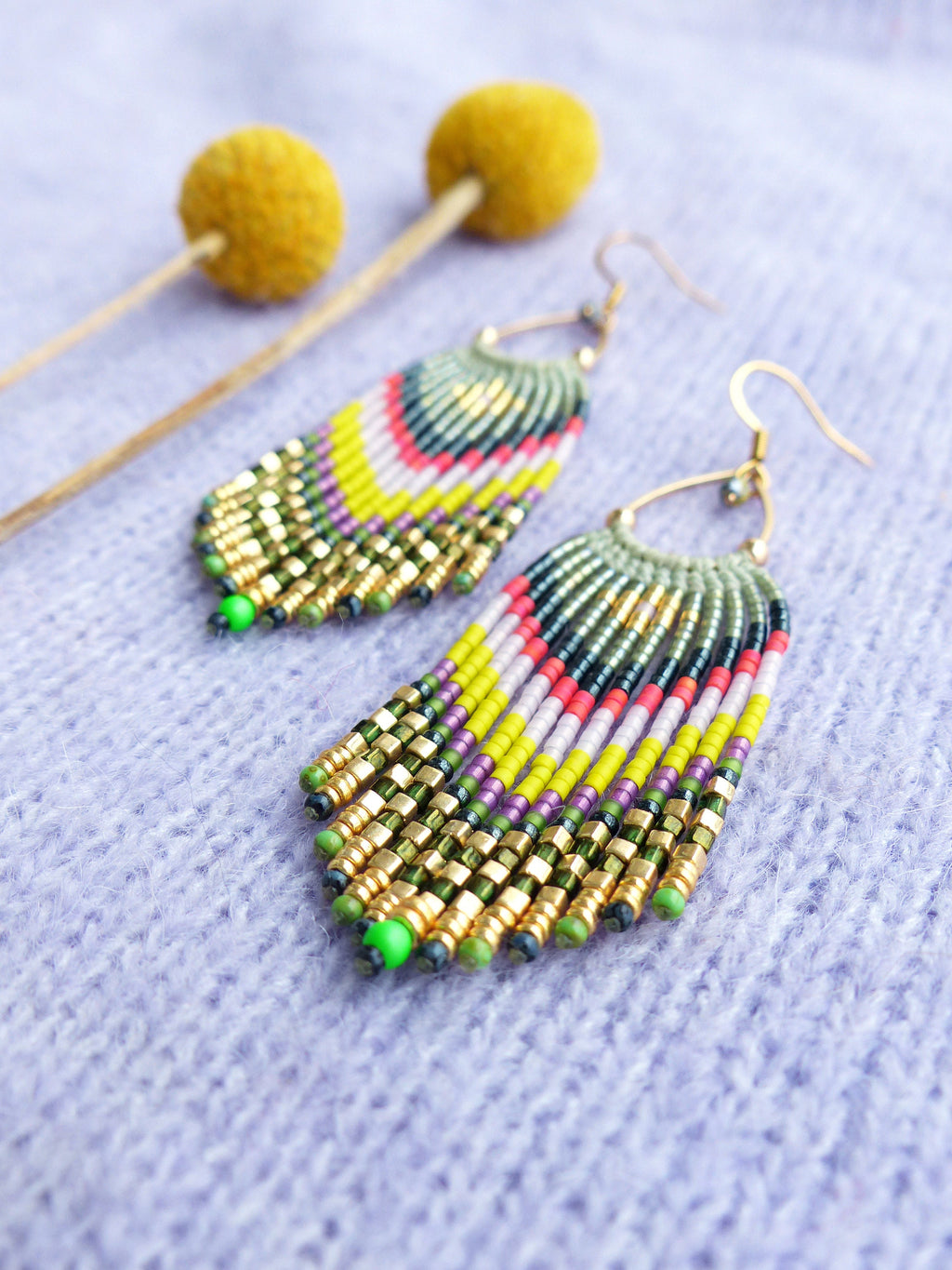 Peut inclure: Une paire de longues boucles d'oreilles en perles colorées avec des accents dorés. Les boucles d'oreilles sont faites avec une variété de perles, y compris le vert, le jaune, le rose et le violet. Les boucles d'oreilles sont suspendues à des crochets dorés.