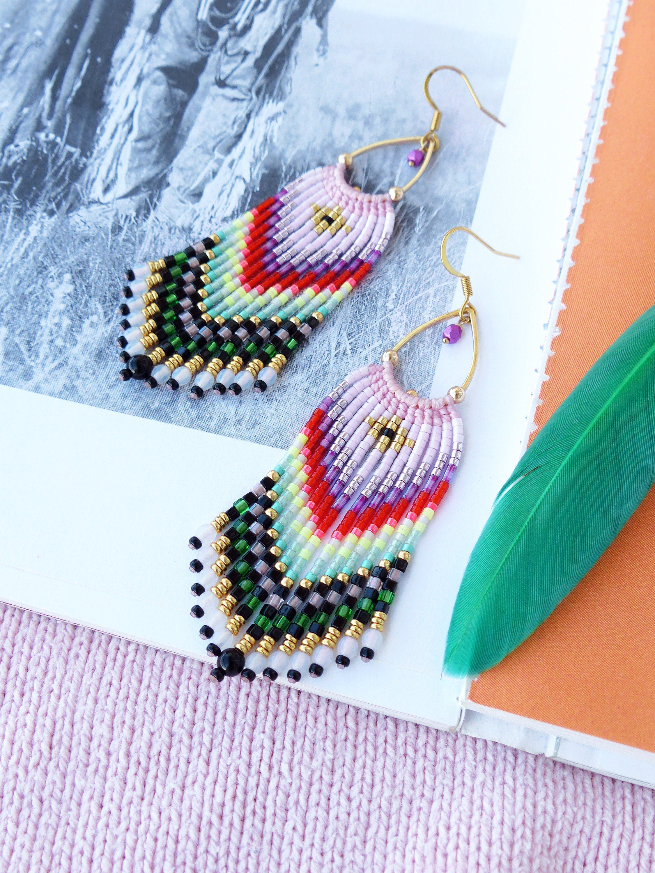 Peut inclure: Une paire de boucles d'oreilles pendantes en perles colorées avec un schéma de couleurs rose, rouge, vert et noir. Les boucles d'oreilles sont faites de petites perles de rocaille et ont un crochet doré.