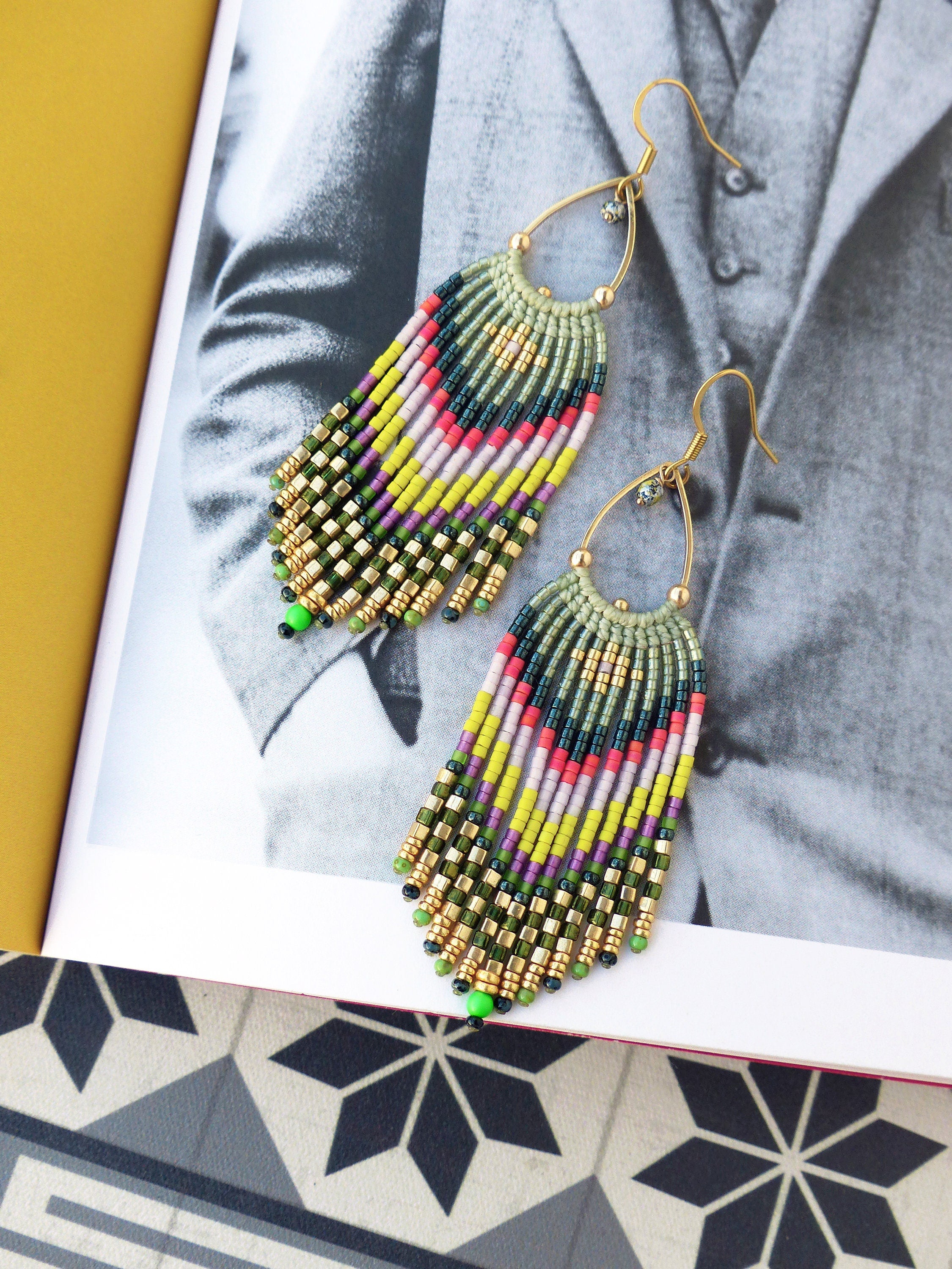 Peut inclure: Une paire de longues boucles d'oreilles en perles colorées avec un anneau en or et des accents verts. Les boucles d'oreilles sont faites avec une variété de perles, y compris le vert, le jaune, le rose et le noir.