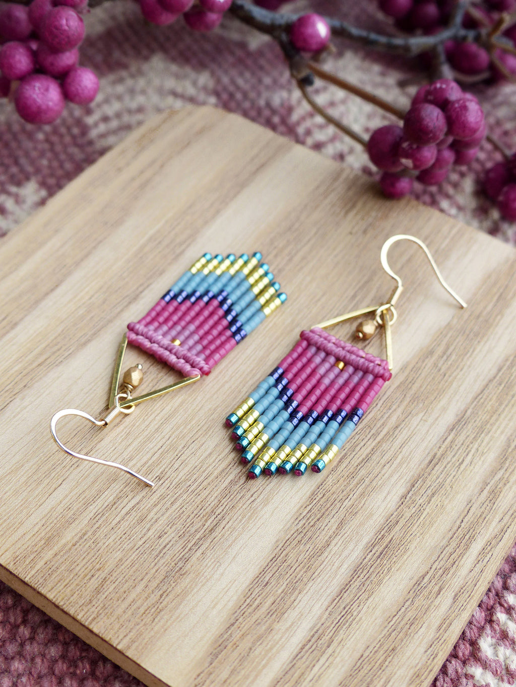 Peut inclure: Une paire de boucles d'oreilles en forme de triangle, composées de perles roses, bleues et dorées. Les boucles d'oreilles sont suspendues à des crochets dorés.