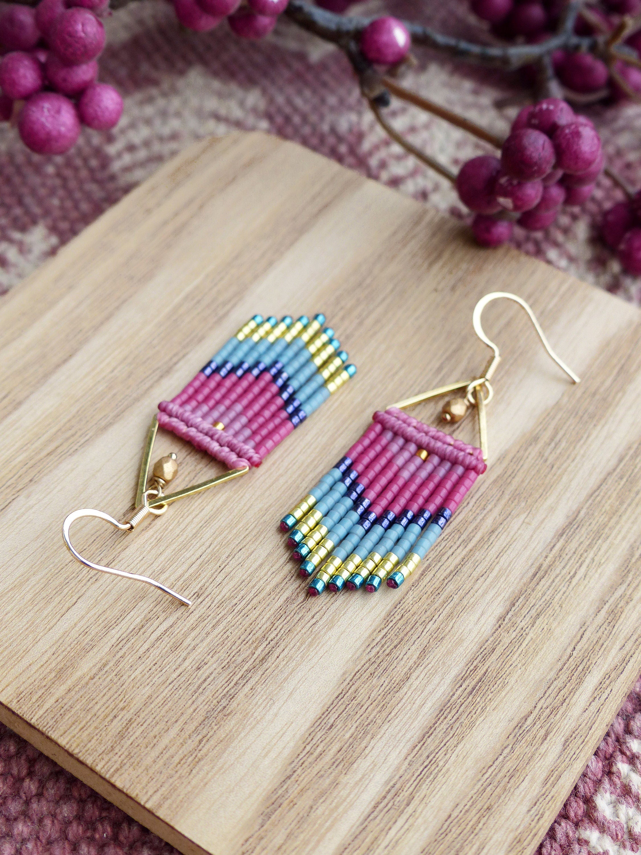 Peut inclure: Une paire de boucles d'oreilles en forme de triangle, composées de perles roses, bleues et dorées. Les boucles d'oreilles sont suspendues à des crochets dorés.