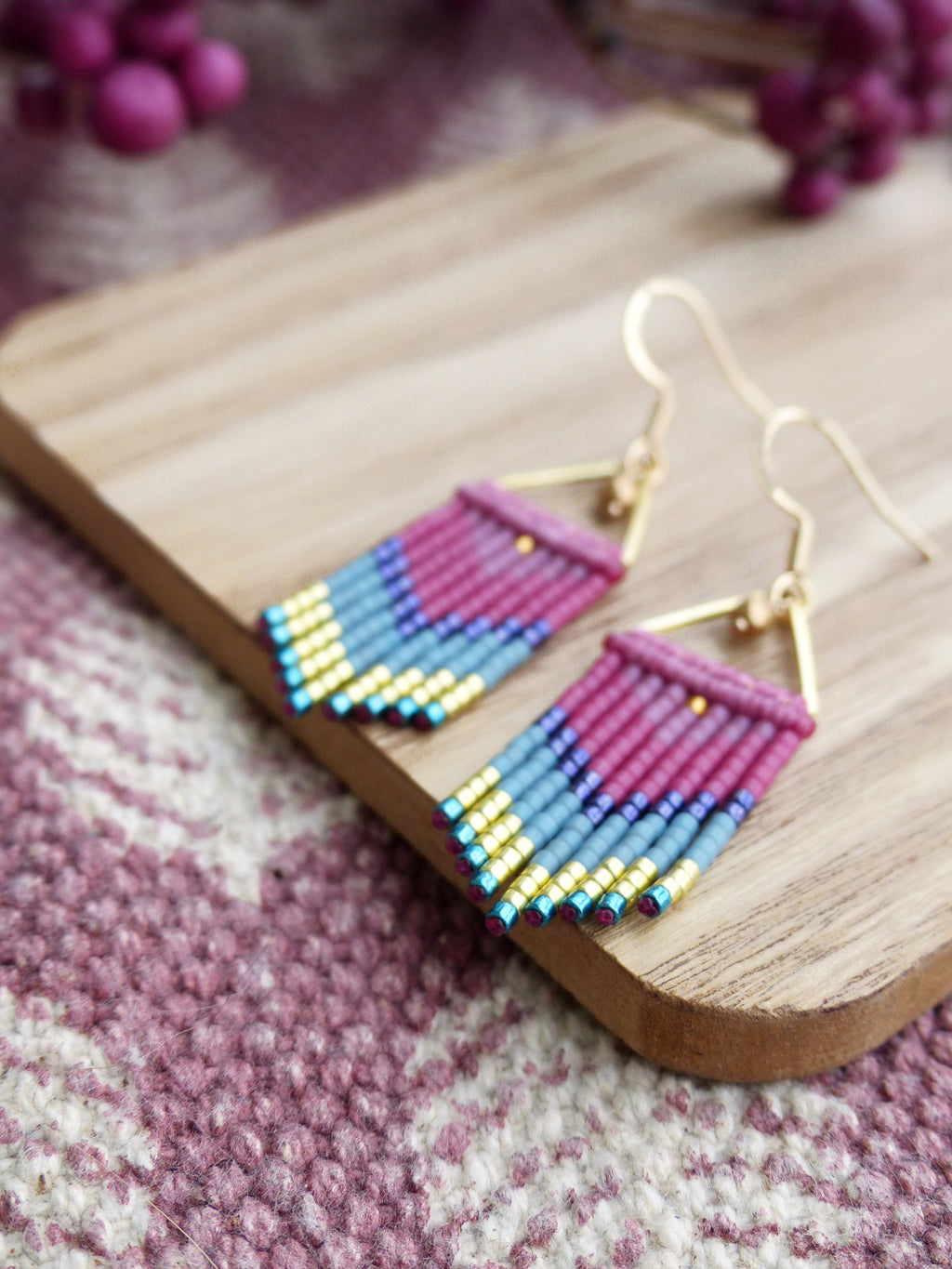 Peut inclure: Une paire de boucles d'oreilles pendantes avec un motif géométrique. Les boucles d'oreilles sont faites de petites perles dans des tons de rose, bleu et or. Les boucles d'oreilles sont suspendues à des crochets dorés.