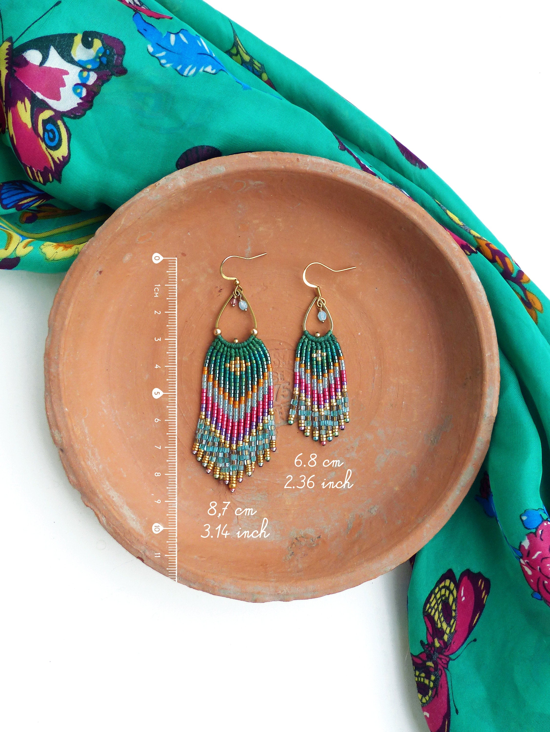 Peut inclure: Une paire de boucles d'oreilles pendantes en perles vertes, bleues et roses avec des crochets dorés. Les boucles d'oreilles mesurent 8,7 cm de long et 6,8 cm de large.