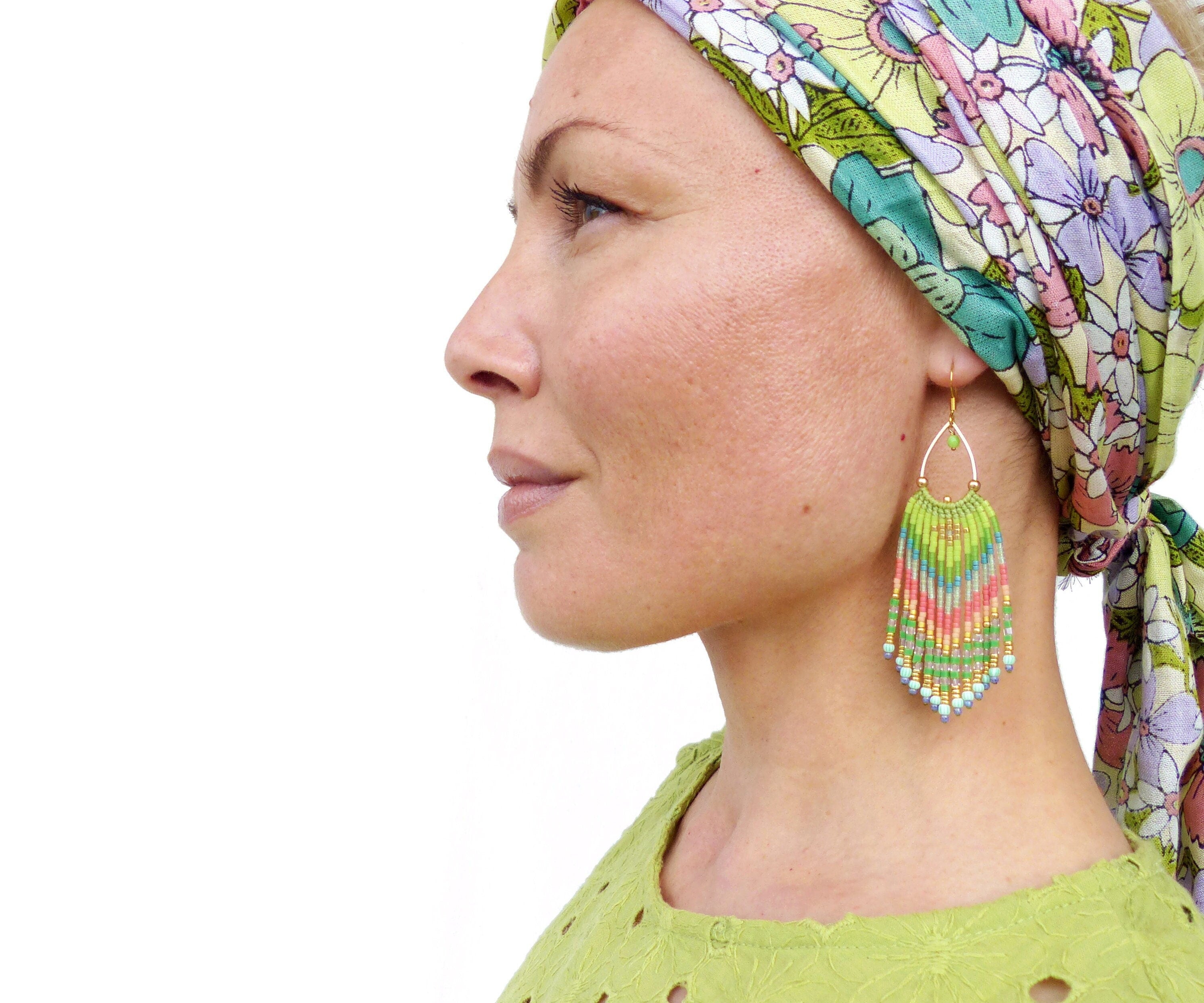 Peut inclure: Une femme portant un bandeau floral et des boucles d'oreilles en perles vertes. Les boucles d'oreilles sont longues et pendantes, avec un mélange de perles vertes, bleues et roses.
