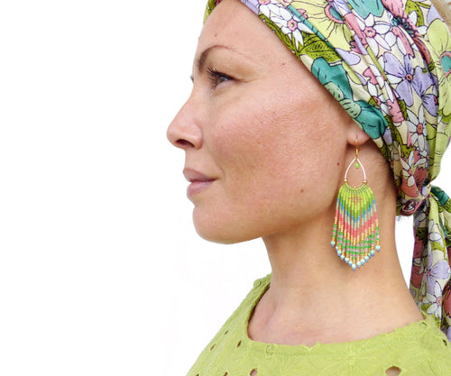 Peut inclure: Une femme portant un bandeau floral et des boucles d'oreilles en perles vertes. Les boucles d'oreilles sont longues et pendantes, avec un mélange de perles vertes, bleues et roses.