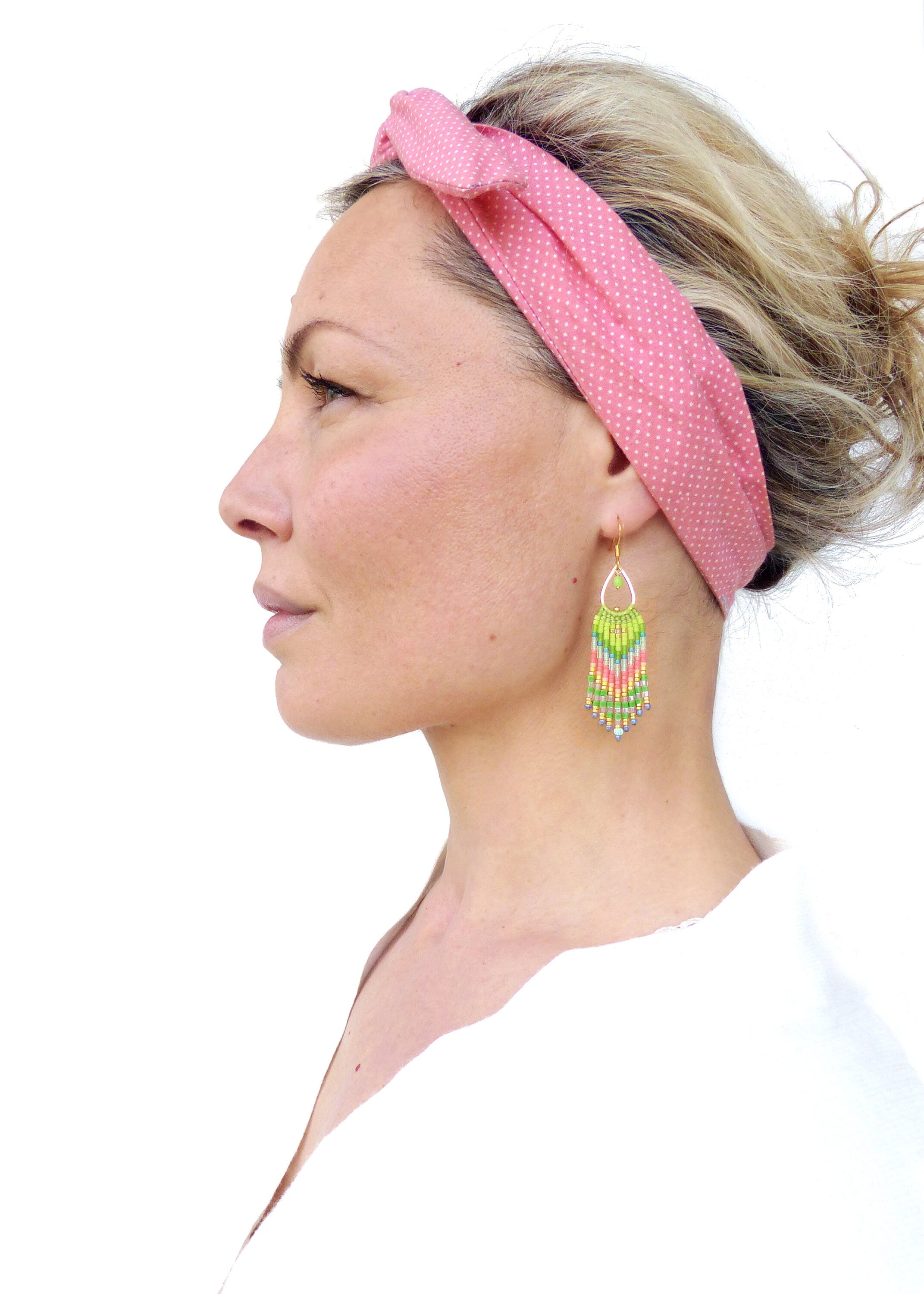 Peut inclure: Une femme portant un bandeau à pois rose et des boucles d'oreilles en perles colorées. Les boucles d'oreilles sont longues et pendantes, avec une forme de larme en haut.