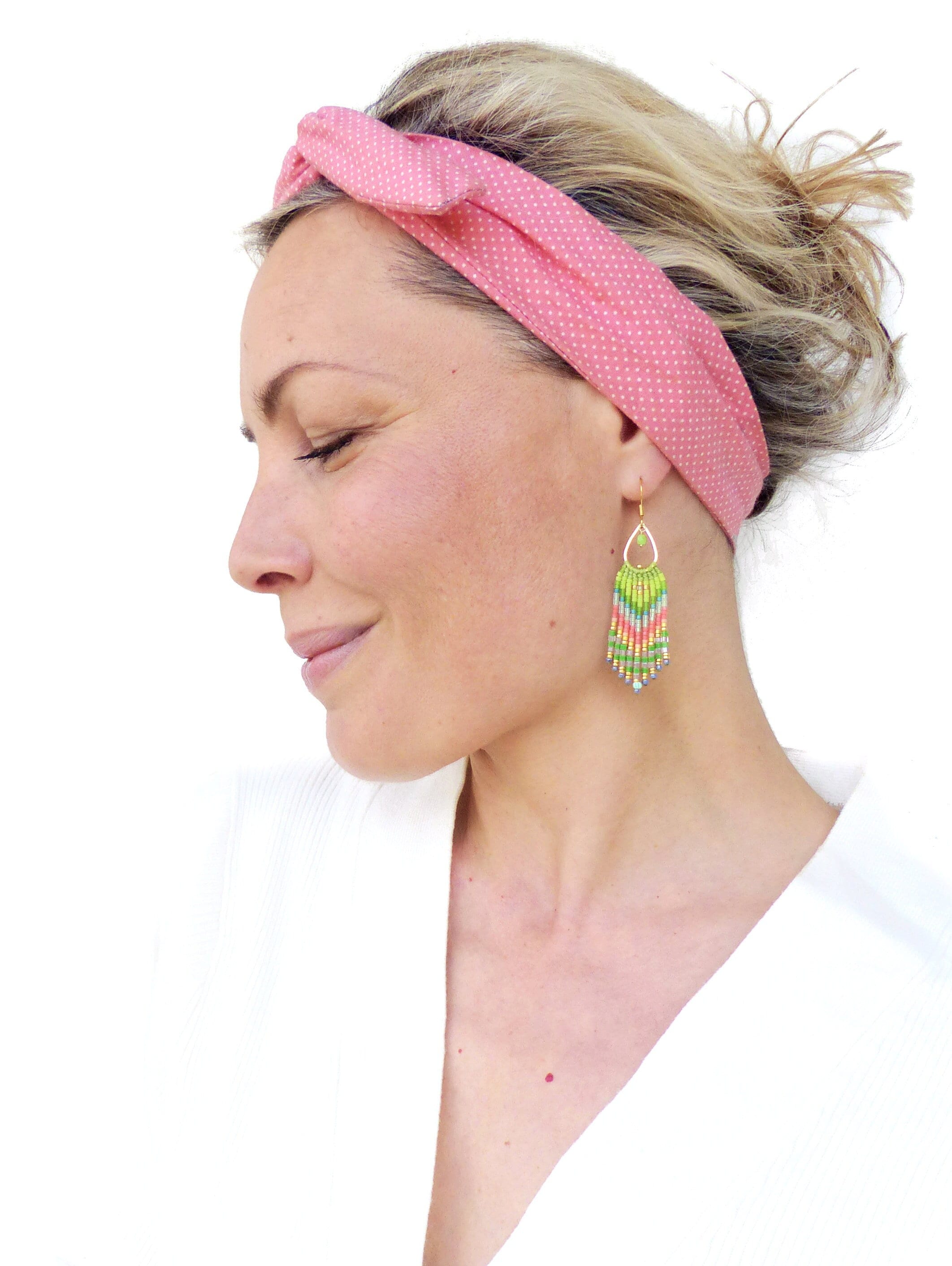 Peut inclure: Une femme portant un bandeau rose à pois blancs et une paire de boucles d'oreilles en perles colorées. Les boucles d'oreilles sont longues et pendantes, avec un sommet en forme de larme et une frange de perles.