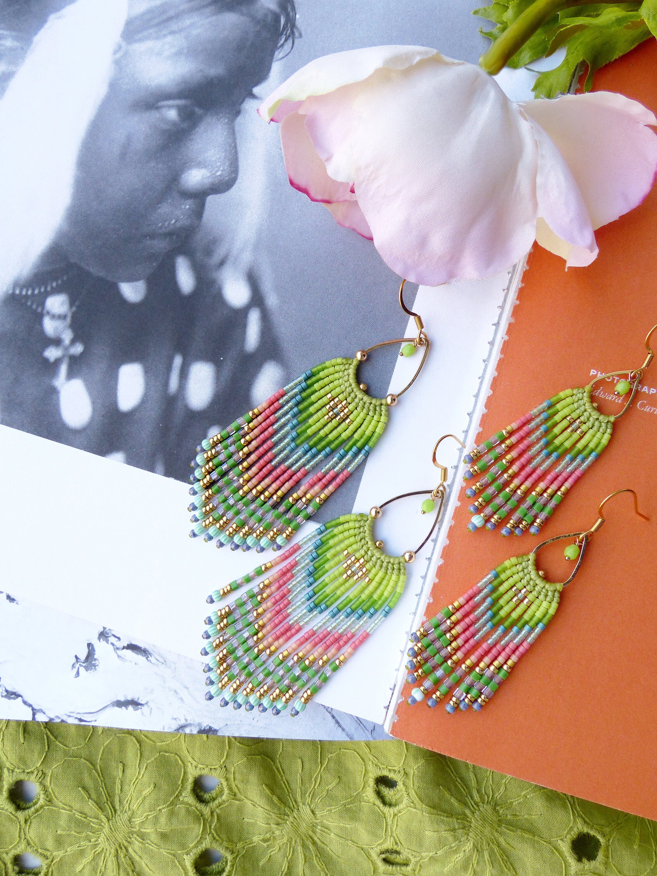 Peut inclure: Une paire de longues boucles d'oreilles en perles avec un design en frange. Les boucles d'oreilles sont faites de perles vertes, roses, bleues et dorées. Les boucles d'oreilles sont suspendues à un fil d'or.