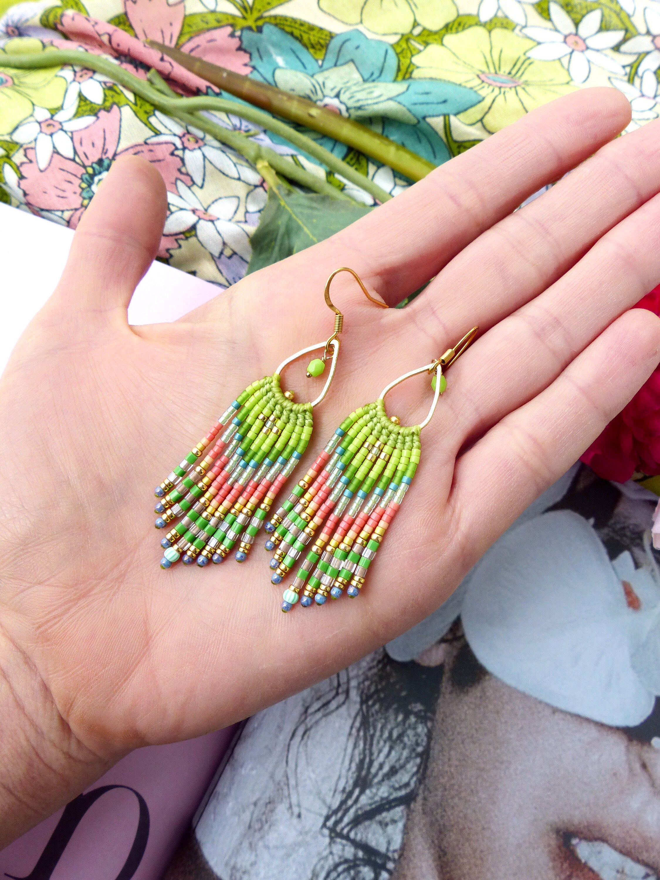 Peut inclure: Une paire de longues boucles d'oreilles pendantes en perles avec un crochet doré. Les boucles d'oreilles sont faites avec une variété de couleurs, y compris le vert, le rose et l'argent.