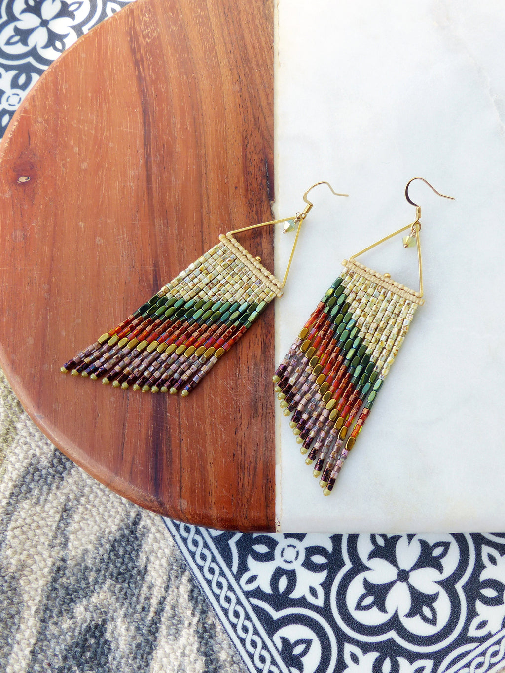 Peut inclure: Une paire de longues boucles d'oreilles en perles avec une forme triangulaire et une finition dorée. Les boucles d'oreilles présentent un design multicolore avec des nuances de brun, d'orange, de vert et d'or.