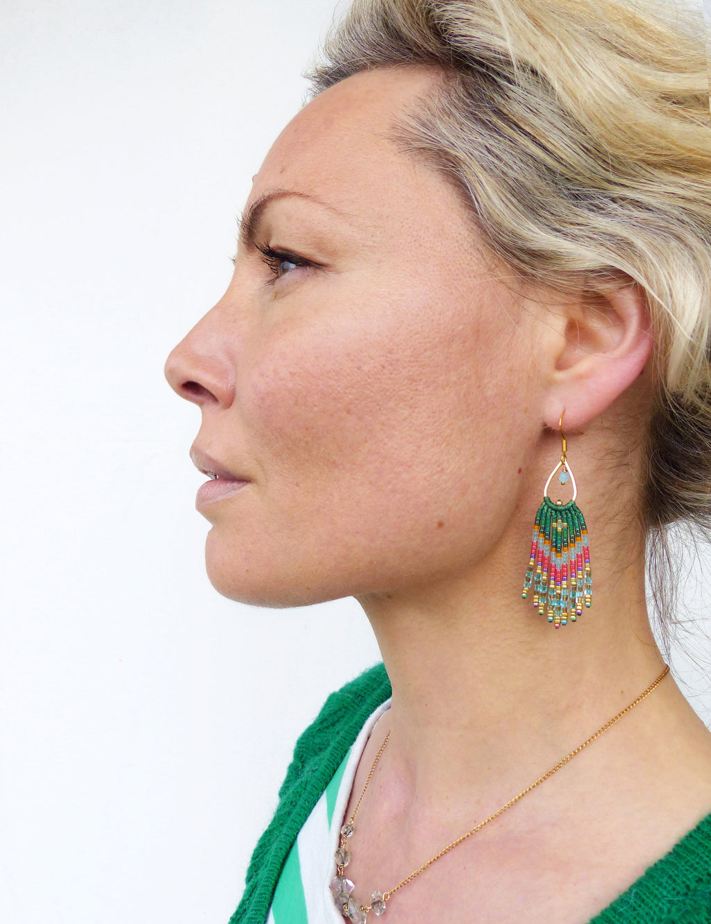 Peut inclure: Une femme portant une chemise rayée verte et blanche avec un collier de chaîne en or et des boucles d'oreilles en perles vertes. Les boucles d'oreilles sont longues et pendantes, avec un motif vert, rose et blanc.