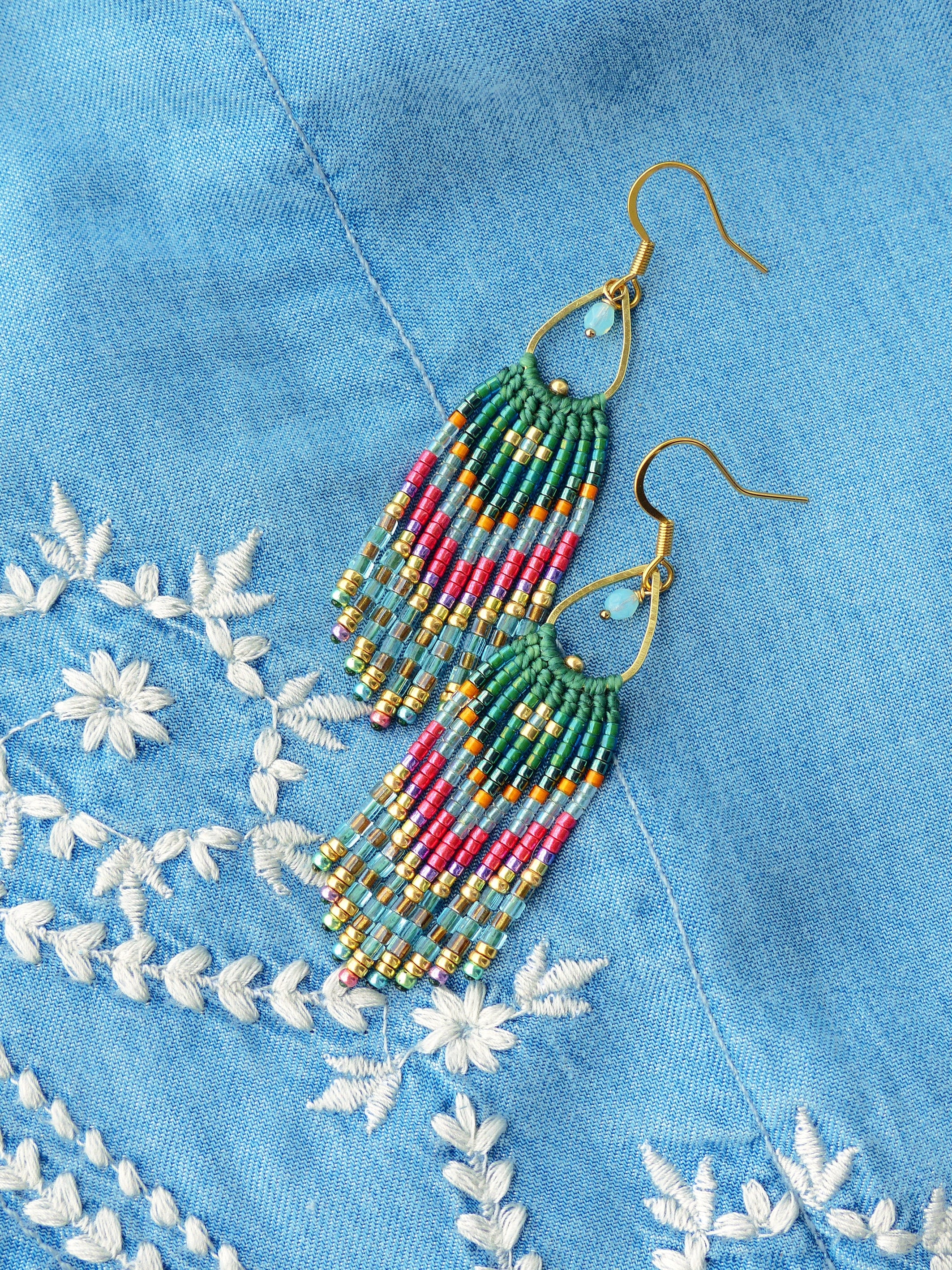 Peut inclure: Une paire de longues boucles d'oreilles en perles avec un crochet doré et un motif turquoise et rose. Les boucles d'oreilles sont suspendues sur un fond en jean bleu.