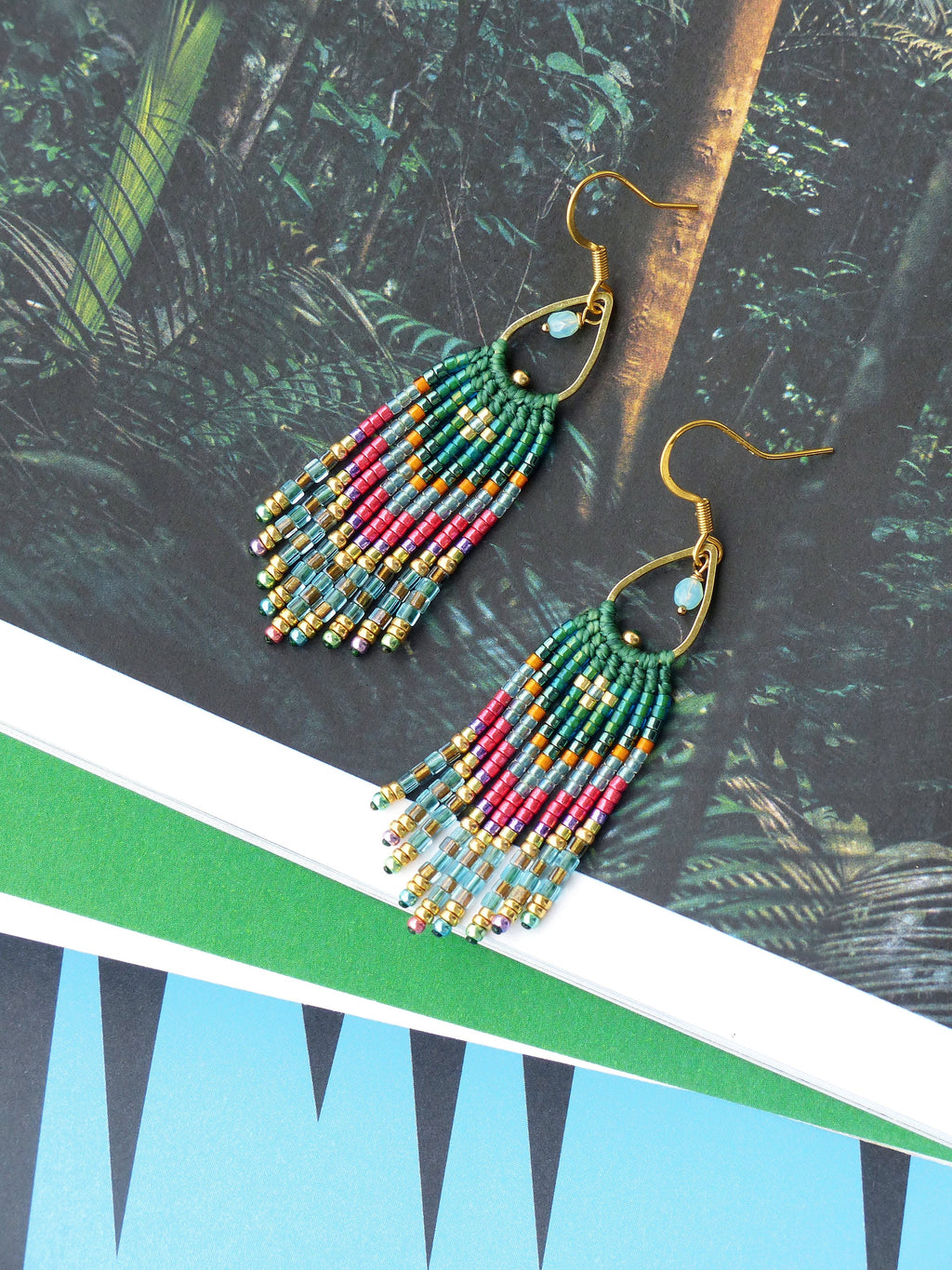 Peut inclure: Une paire de boucles d'oreilles en forme de glands, composées de perles vertes, dorées et multicolores, avec des crochets dorés.
