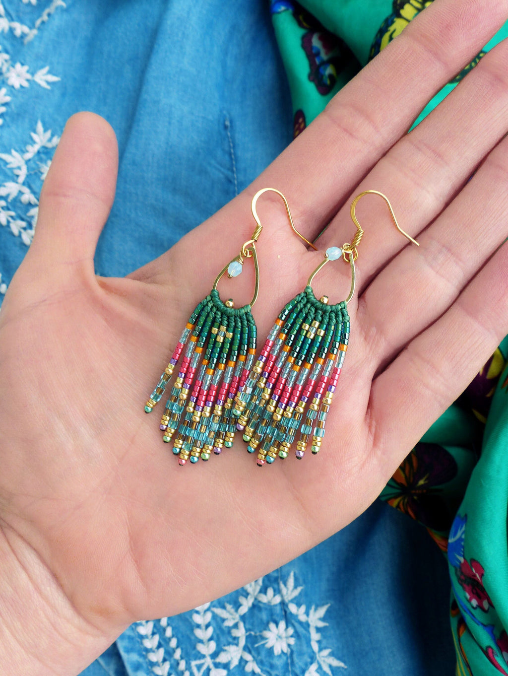 Peut inclure: Une paire de boucles d'oreilles pendantes en perles vertes, bleues et roses avec des crochets dorés et une perle transparente en haut.