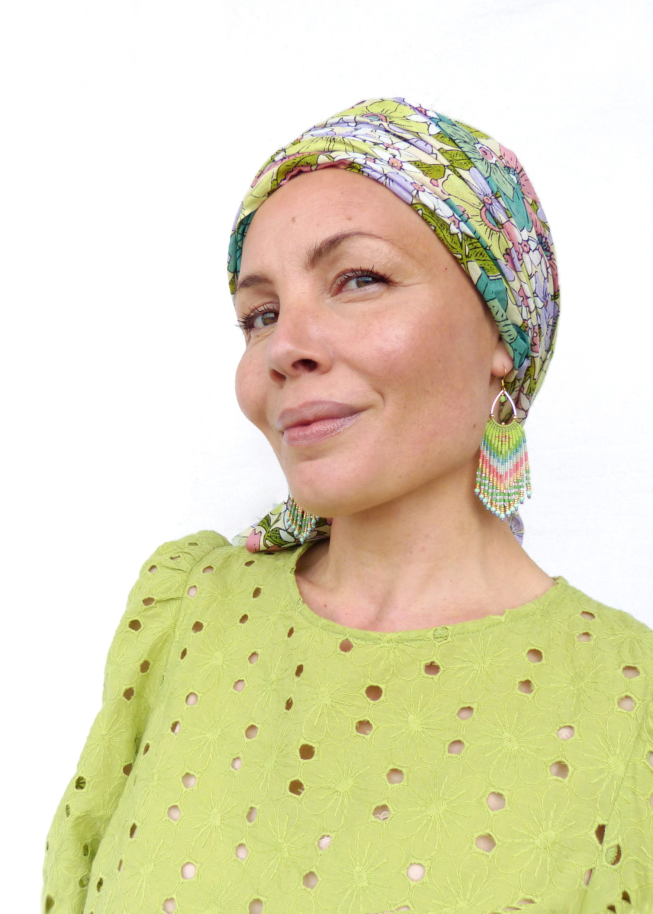 Peut inclure: Une femme aux cheveux courts porte un foulard à fleurs vert et une blouse verte à œillets. Elle porte de longues boucles d'oreilles en perles colorées.