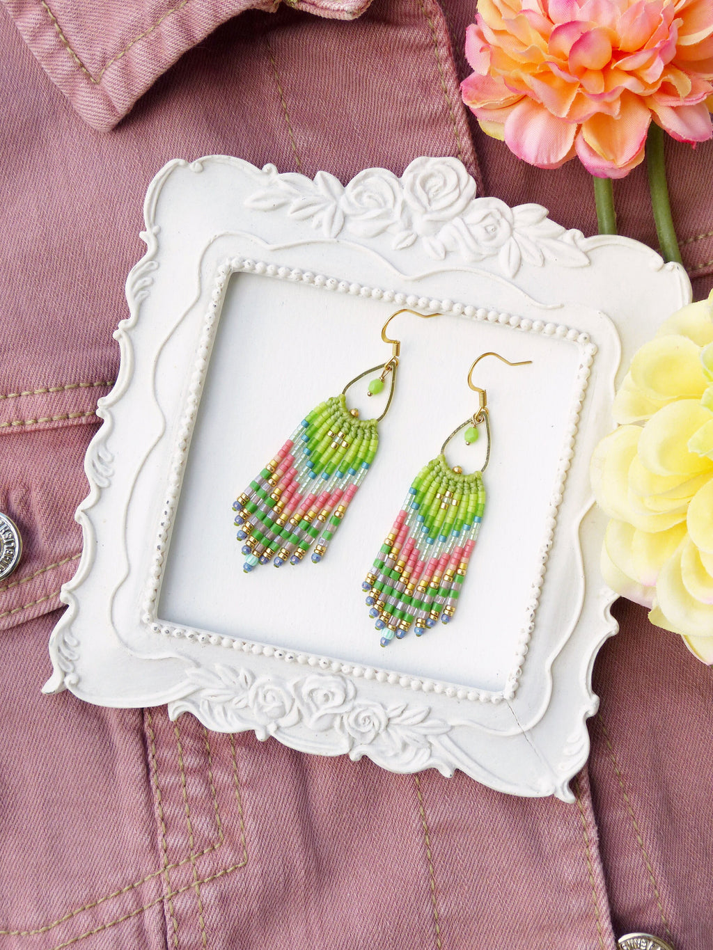 Peut inclure: Une paire de boucles d'oreilles pendantes en perles vertes, roses et bleues avec des crochets dorés. Les boucles d'oreilles sont présentées dans un cadre blanc à motif floral.