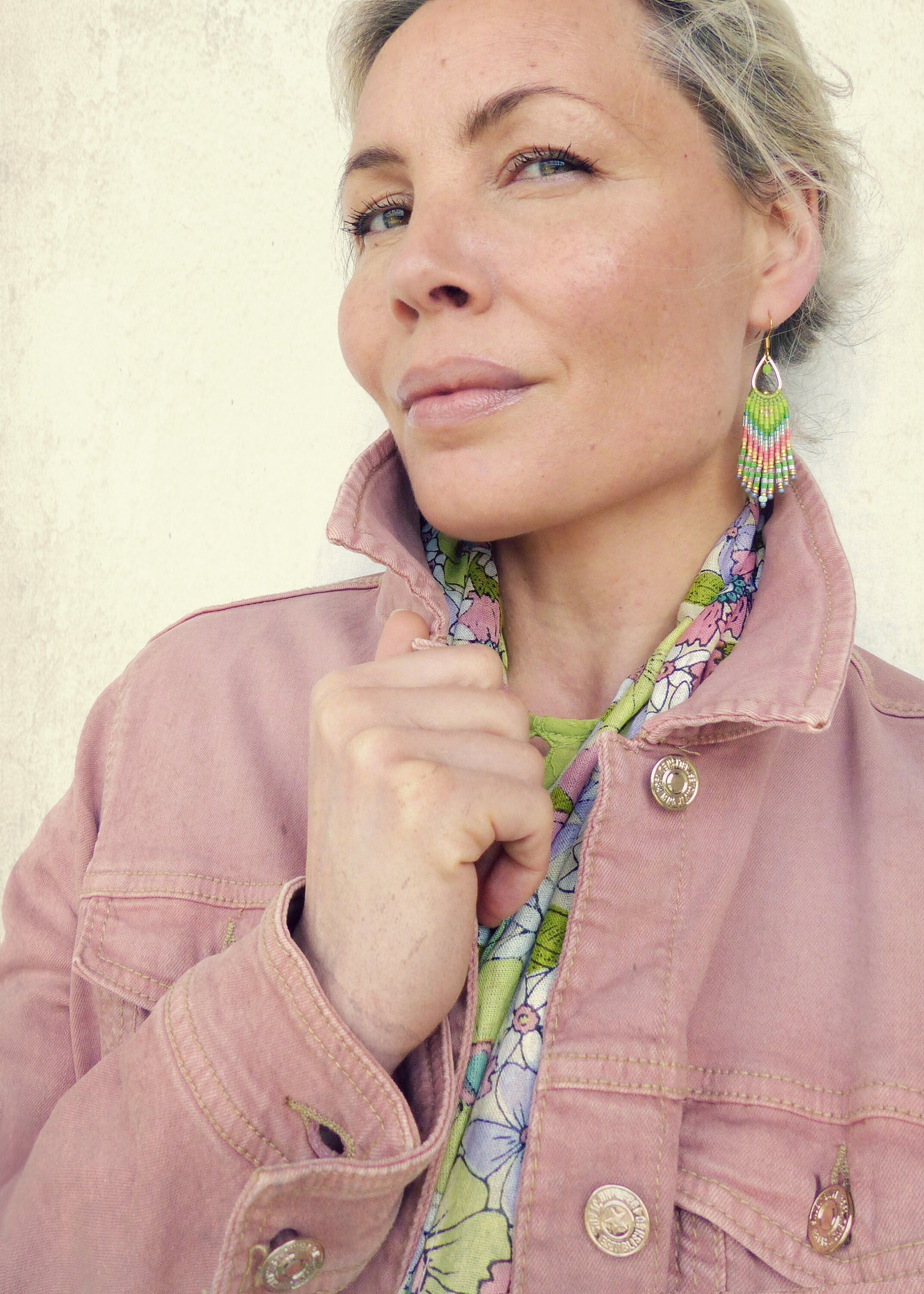 Peut inclure: Une femme portant une veste en jean rose avec une écharpe florale et des boucles d'oreilles en perles vertes.