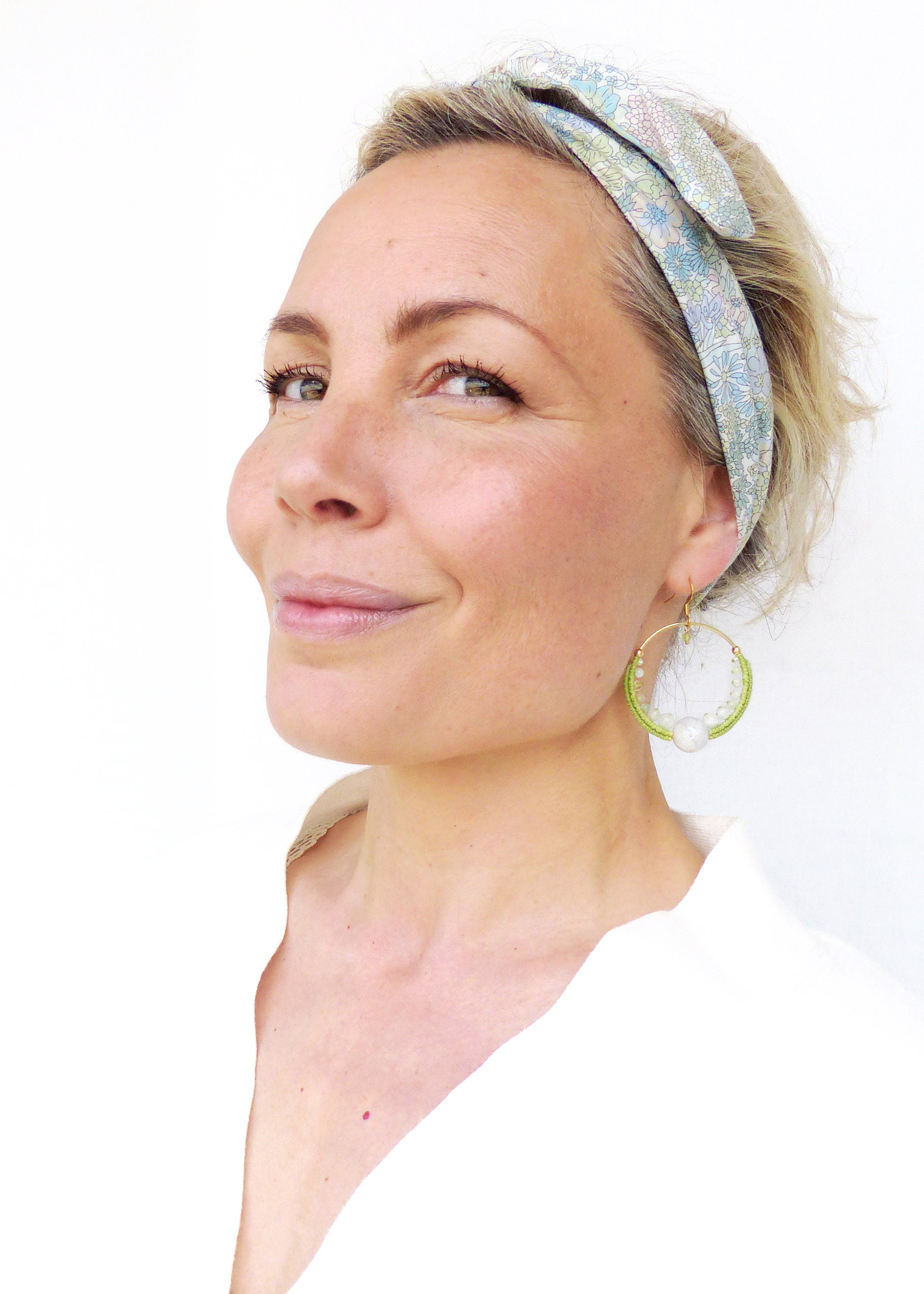 Peut inclure: Une femme portant une chemise blanche et un bandeau floral avec une boucle d'oreille en forme de cercle en perles vertes et blanches.