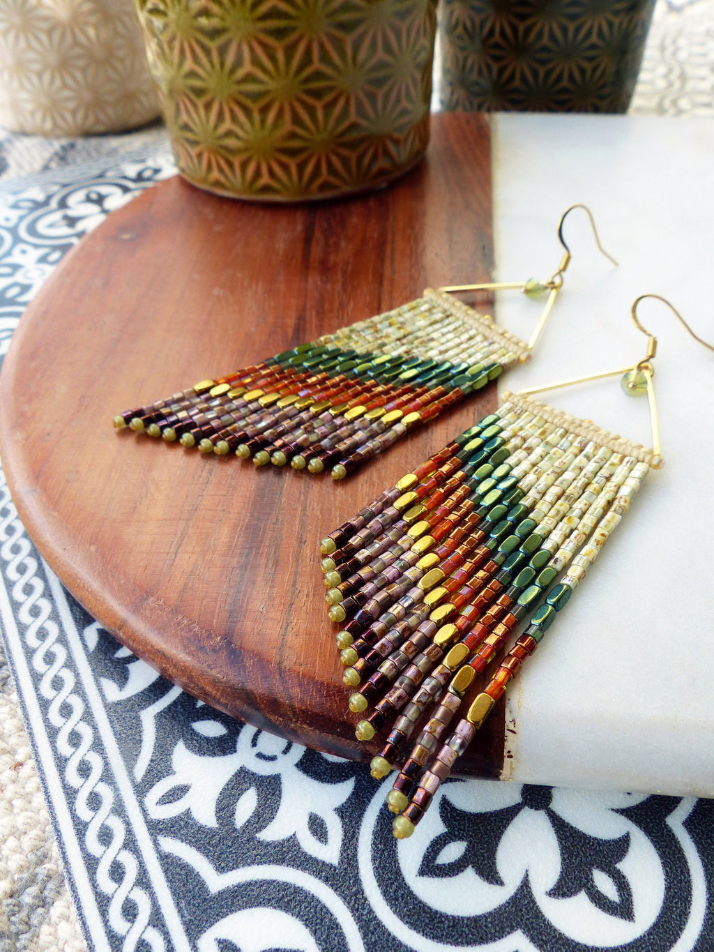 Peut inclure: Une paire de longues boucles d'oreilles en perles avec une forme triangulaire dorée en haut. Les perles sont dans des tons de brun, vert, or et blanc, créant un effet dégradé en couches.