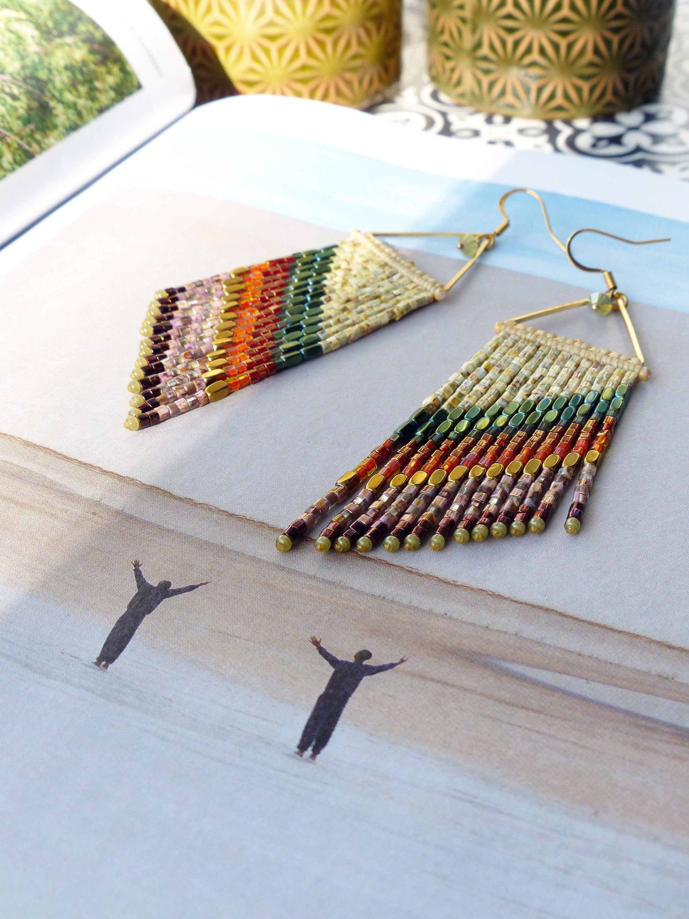 Peut inclure: Une paire de longues boucles d'oreilles en perles avec une forme triangulaire et une frange de perles colorées. Les boucles d'oreilles sont faites avec une variété de couleurs, y compris l'or, le brun, le vert et le rouge.