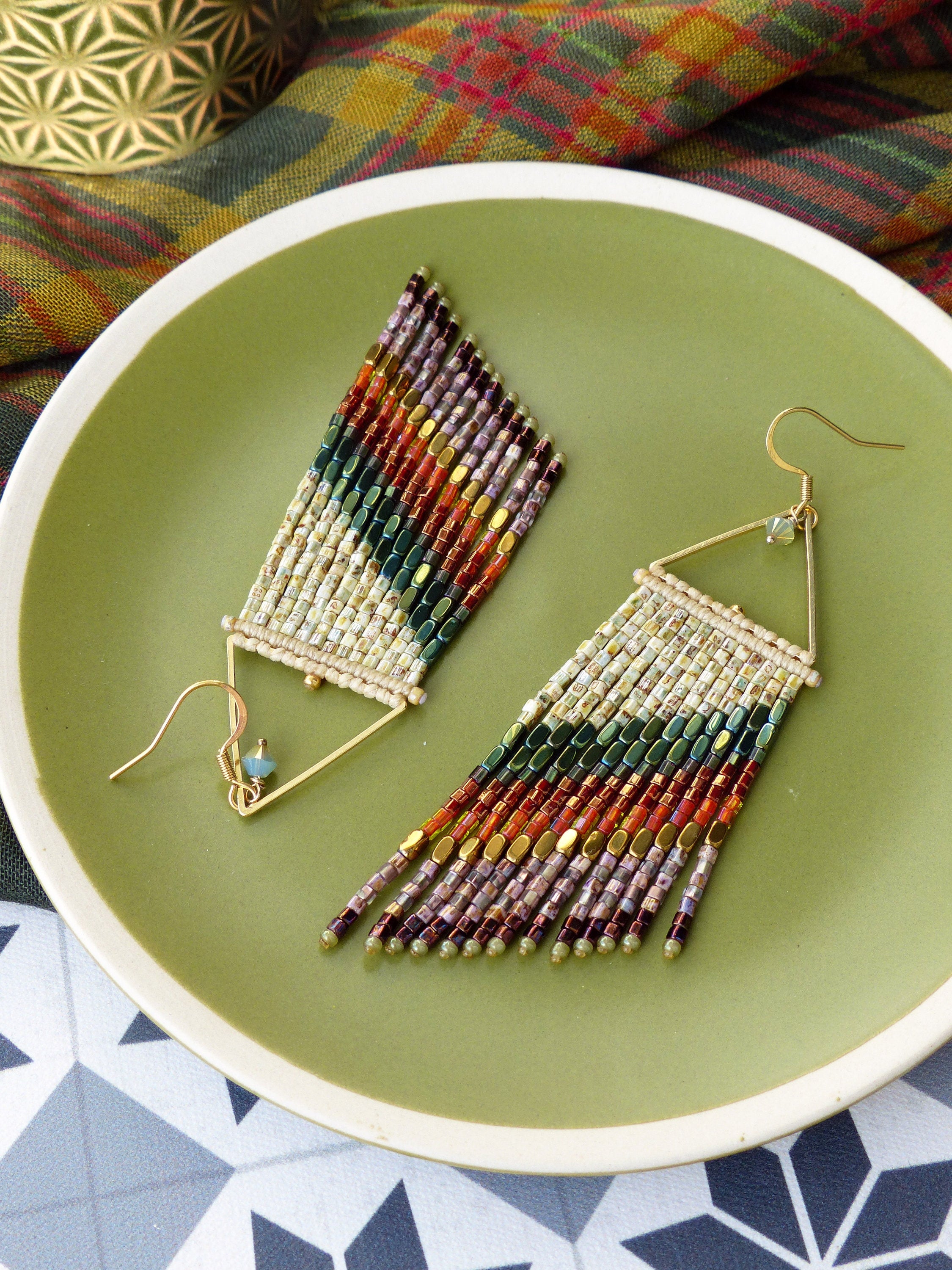 Peut inclure: Une paire de longues boucles d'oreilles en perles avec un motif géométrique. Les boucles d'oreilles sont faites de différentes couleurs, notamment le blanc, l'or, le brun, le rouge et le vert. Les boucles d'oreilles sont suspendues à des tiges triangulaires dorées.