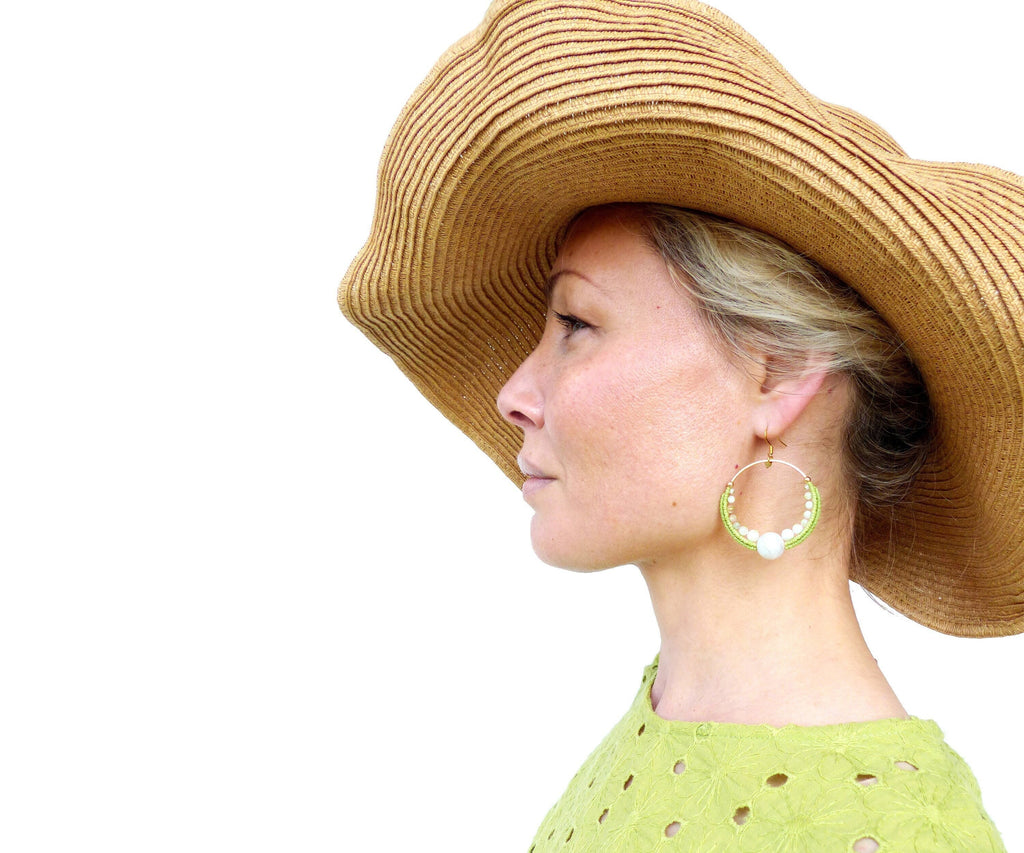 Peut inclure: Une femme portant un chapeau de paille à larges bords et une robe verte à pois blancs. Elle porte de grandes boucles d'oreilles en forme de cerceau avec des perles vertes et blanches.