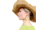 Peut inclure: Une femme portant un chapeau de paille à larges bords et une robe verte à pois blancs. Elle porte de grandes boucles d'oreilles en forme de cerceau avec des perles vertes et blanches.