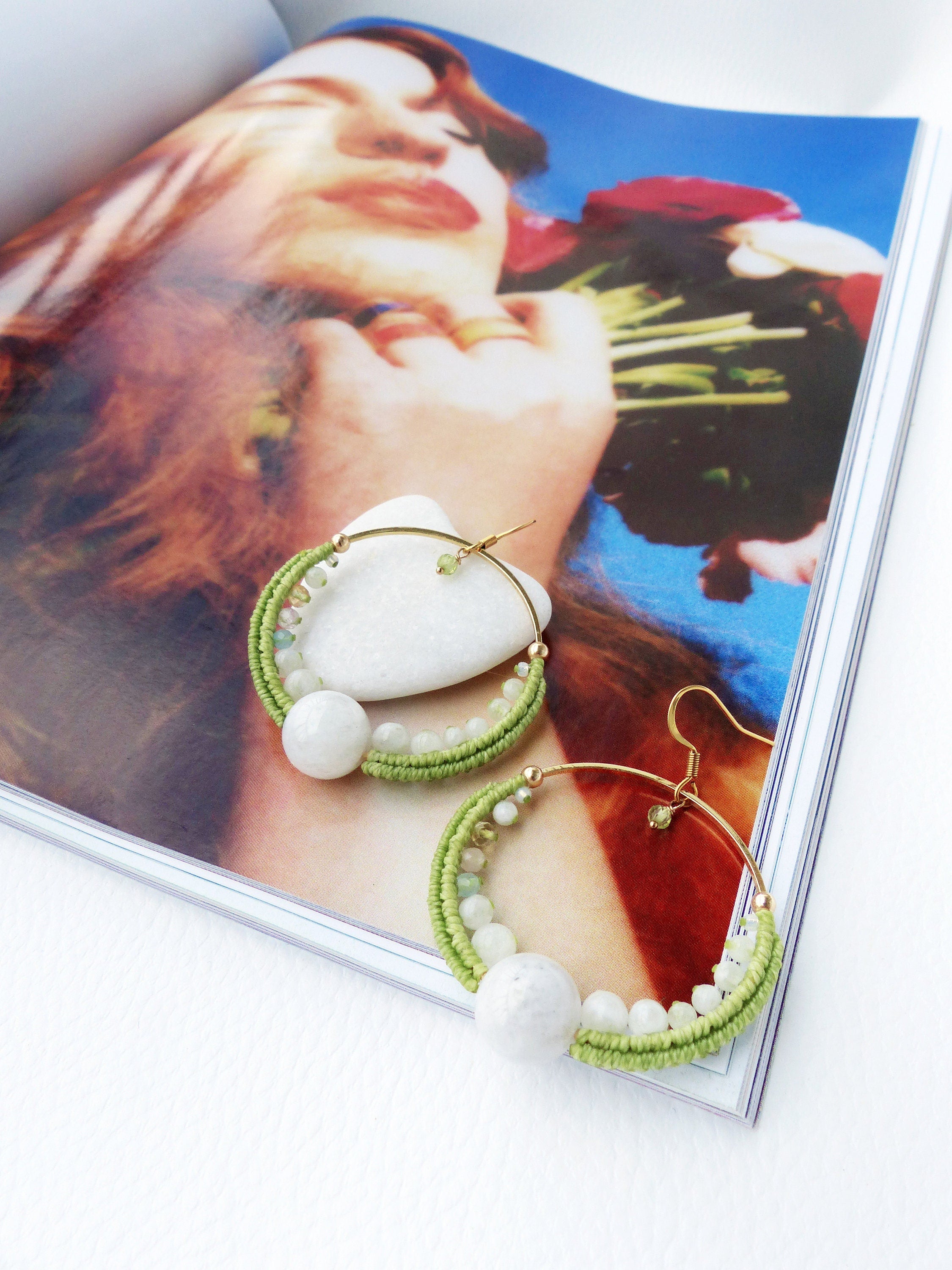 Peut inclure: Une paire de boucles d'oreilles créoles vertes et blanches avec une grosse perle blanche sur chaque créole. Les boucles d'oreilles sont faites de fil vert et de petites perles blanches.