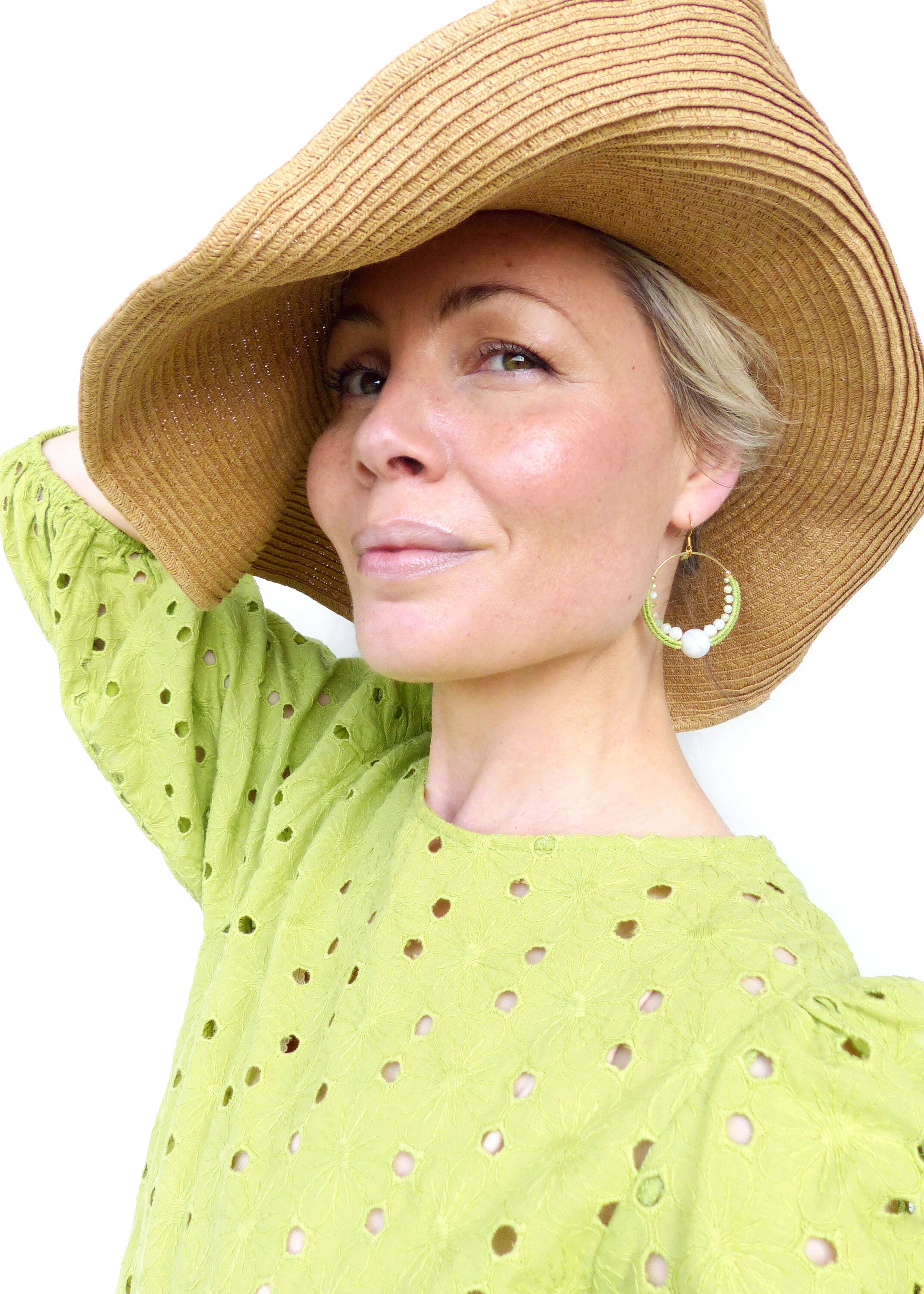 Peut inclure: Une femme portant un chapeau de paille et une blouse verte à œillets avec des boucles d'oreilles en perles blanches et en perles vertes.
